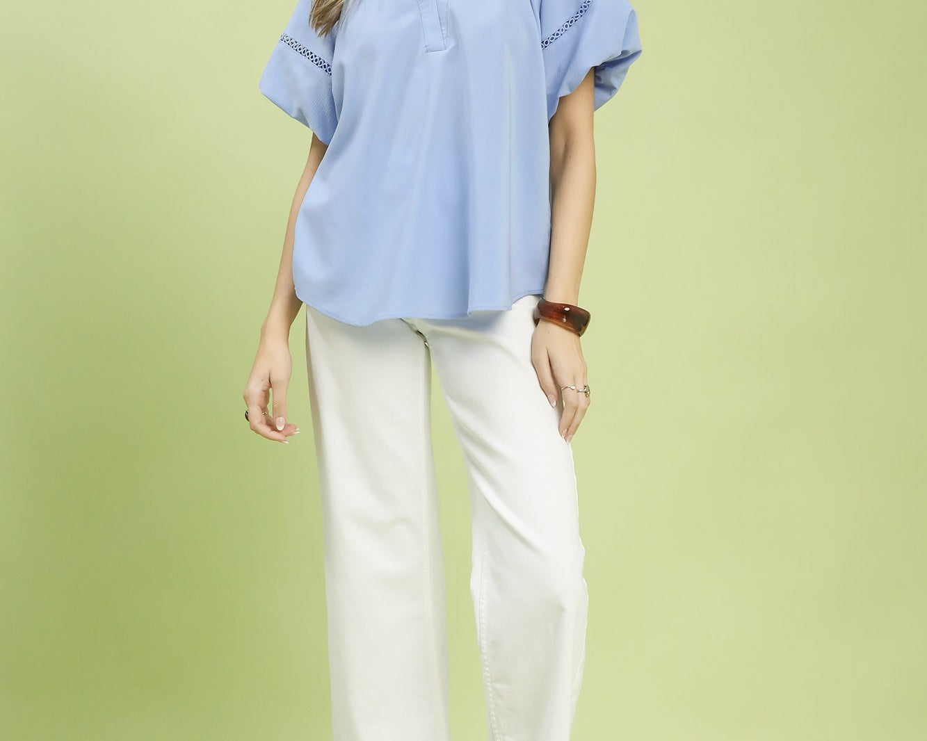 NEWYORKLISTED STYLE COLLECTION: Woman wearing a light blue blouse and white pants on a green background