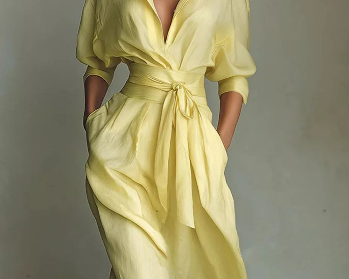 NEWYORKLISTED STYLE COLLECTION: A woman wearing a pale yellow wrap-style midi dress with three-quarter sleeves, a tie waist, and side pockets, photographed against a plain light gray studio background.