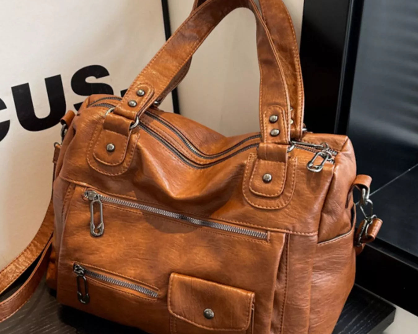NEWYORKLISTED STYLE COLLECTION: Brown leather handbag on a dark surface with a blurred background