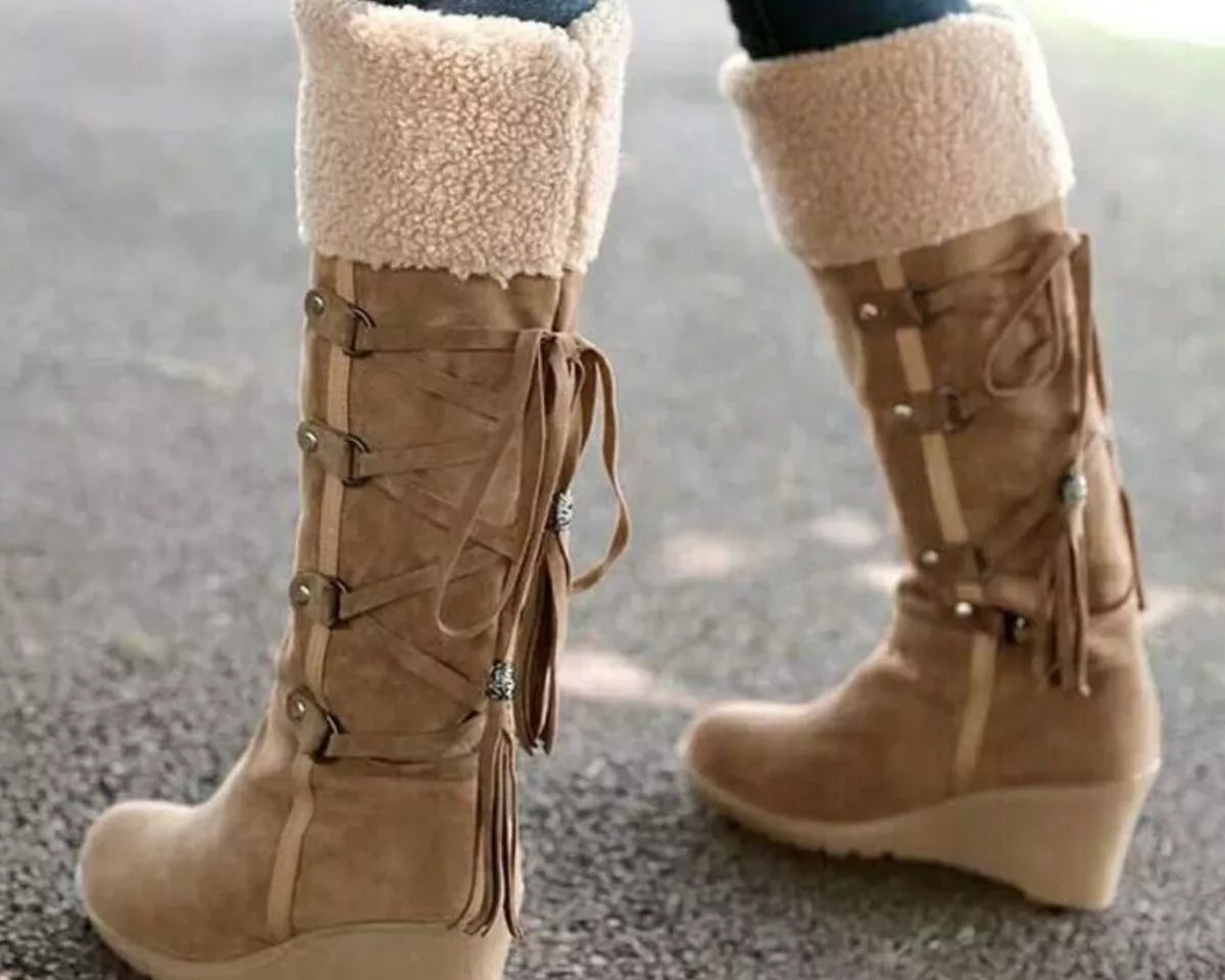 NEWYORKLISTED SHOE COLLECTION: Tan knee-high boots with fringes and white fur lining worn on a blurred background