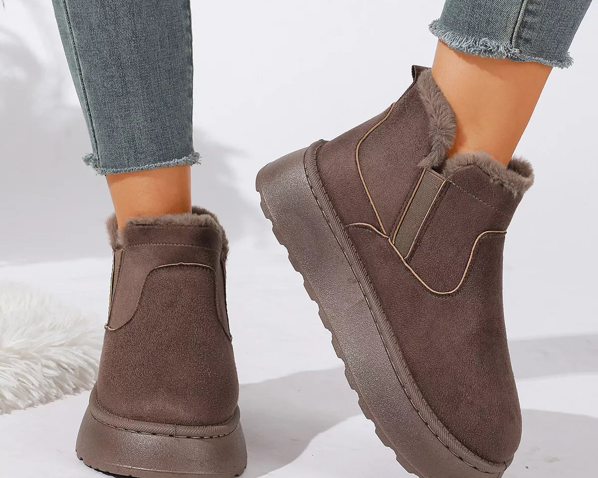 NEWYORKLISTED SHOE COLLECTION: A pair of women's brown suede-like ankle boots with plush faux-fur lining and elastic side panels, shown worn with gray frayed-hem jeans on a white studio background.