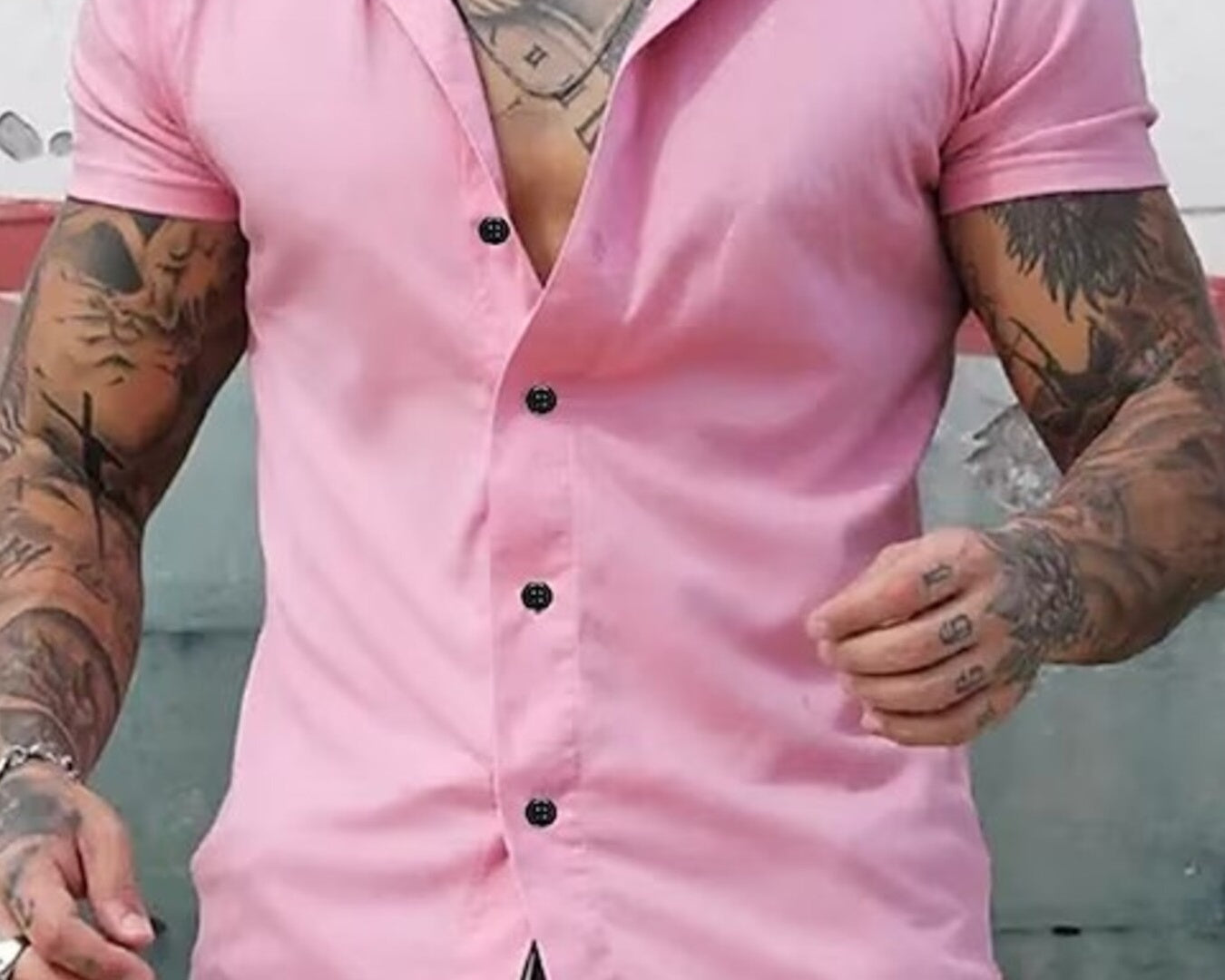 NEWYORKLISTED ATLAS MEN's COLLECTION: Man wearing a pink short-sleeve shirt with black buttons, standing against a neutral background.
