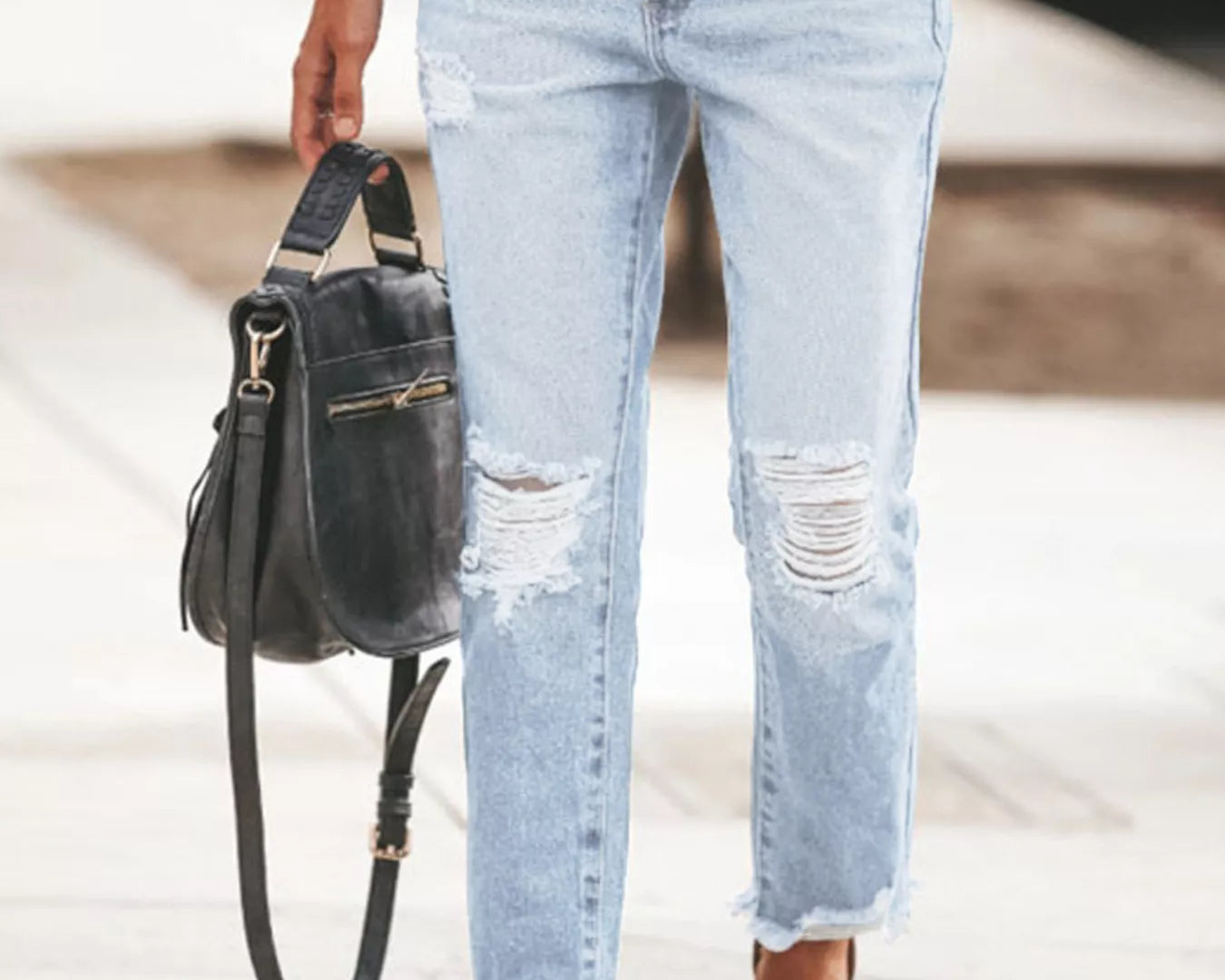 NEWYORKLISTED STYLE COLLECTION: Person wearing light blue distressed jeans holding a black handbag.