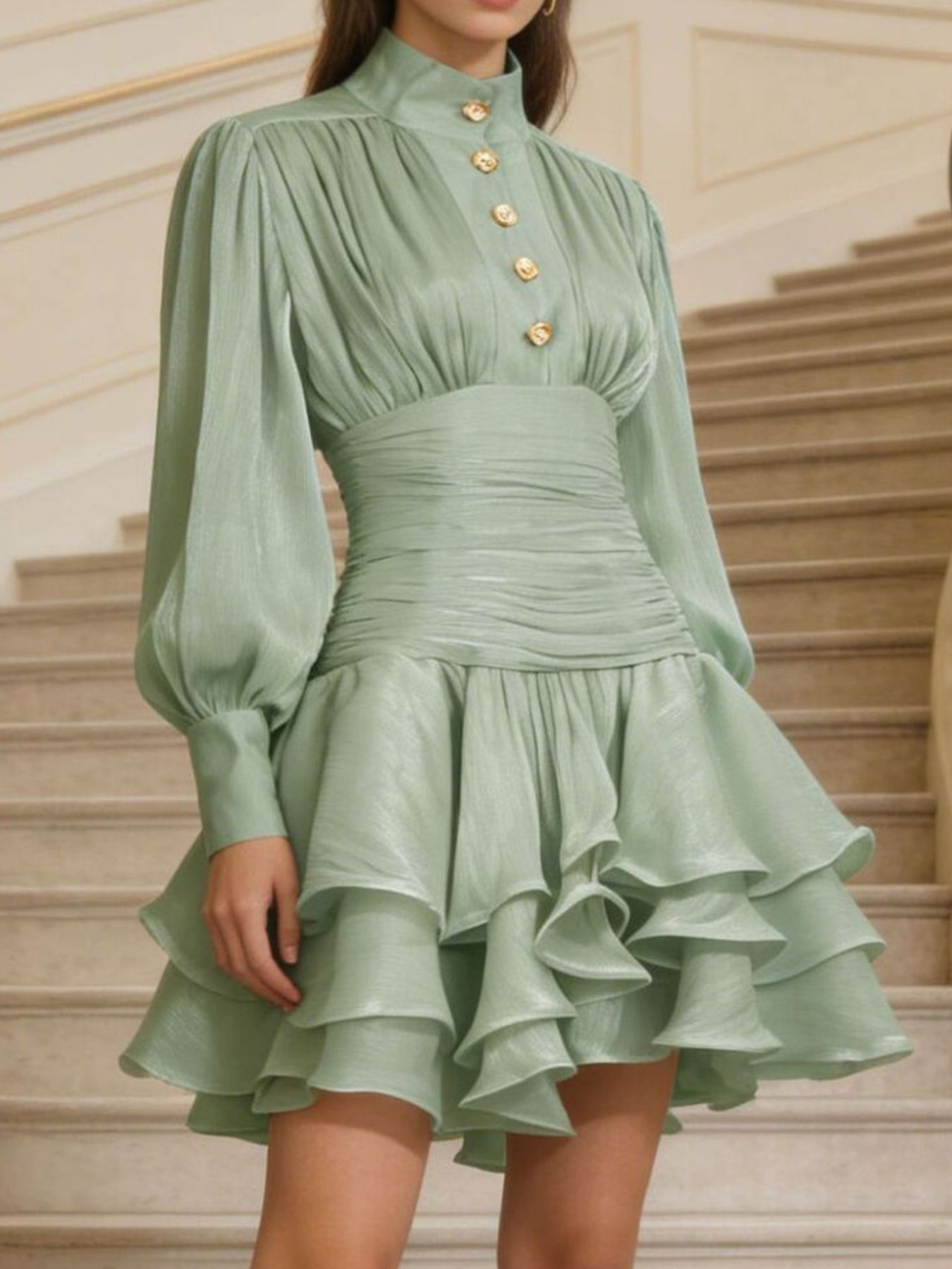 NEWYORKLISTED STYLE COLLECTION: Green dress with long sleeves and ruffled skirt worn by a person on a staircase.