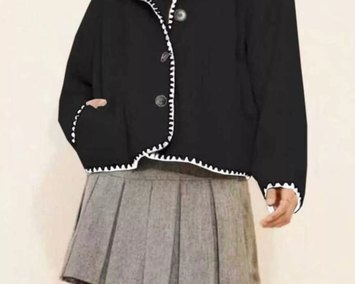 NEWYORKLISTED STYLE COLLECTION: Black jacket with white trim worn over a gray pleated skirt on a plain background