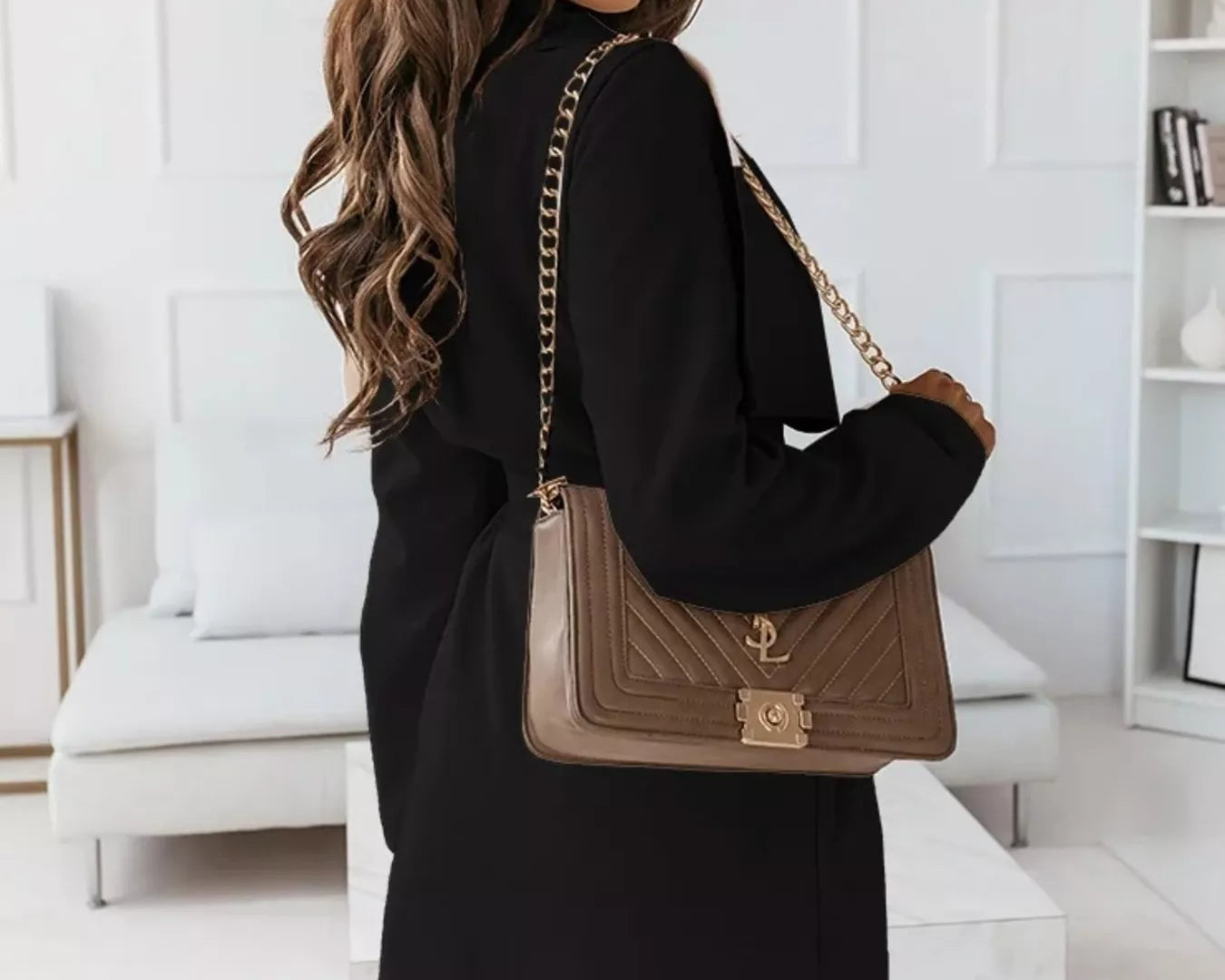 NEWYORKLISTED STYLE COLLECTION: Woman holding a brown handbag with gold chain strap in a modern interior setting