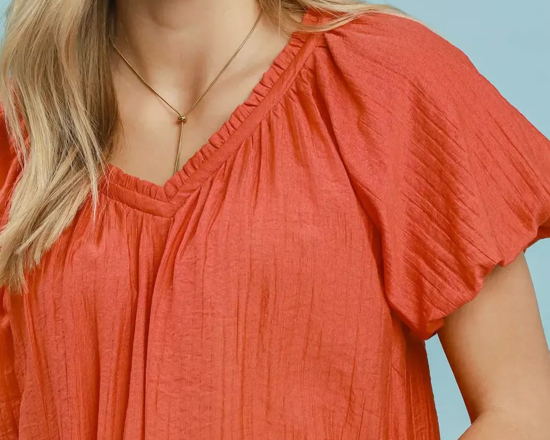 NEWYORKLISTED STYLE COLLECTION: Woman wearing a coral blouse against a light blue background