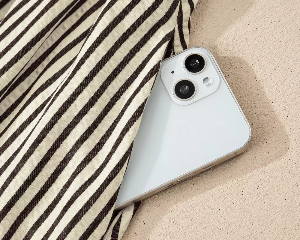 NEWYORKLISTED STYLE COLLECTION: White smartphone with black camera lenses on a sandy surface with striped fabric.
