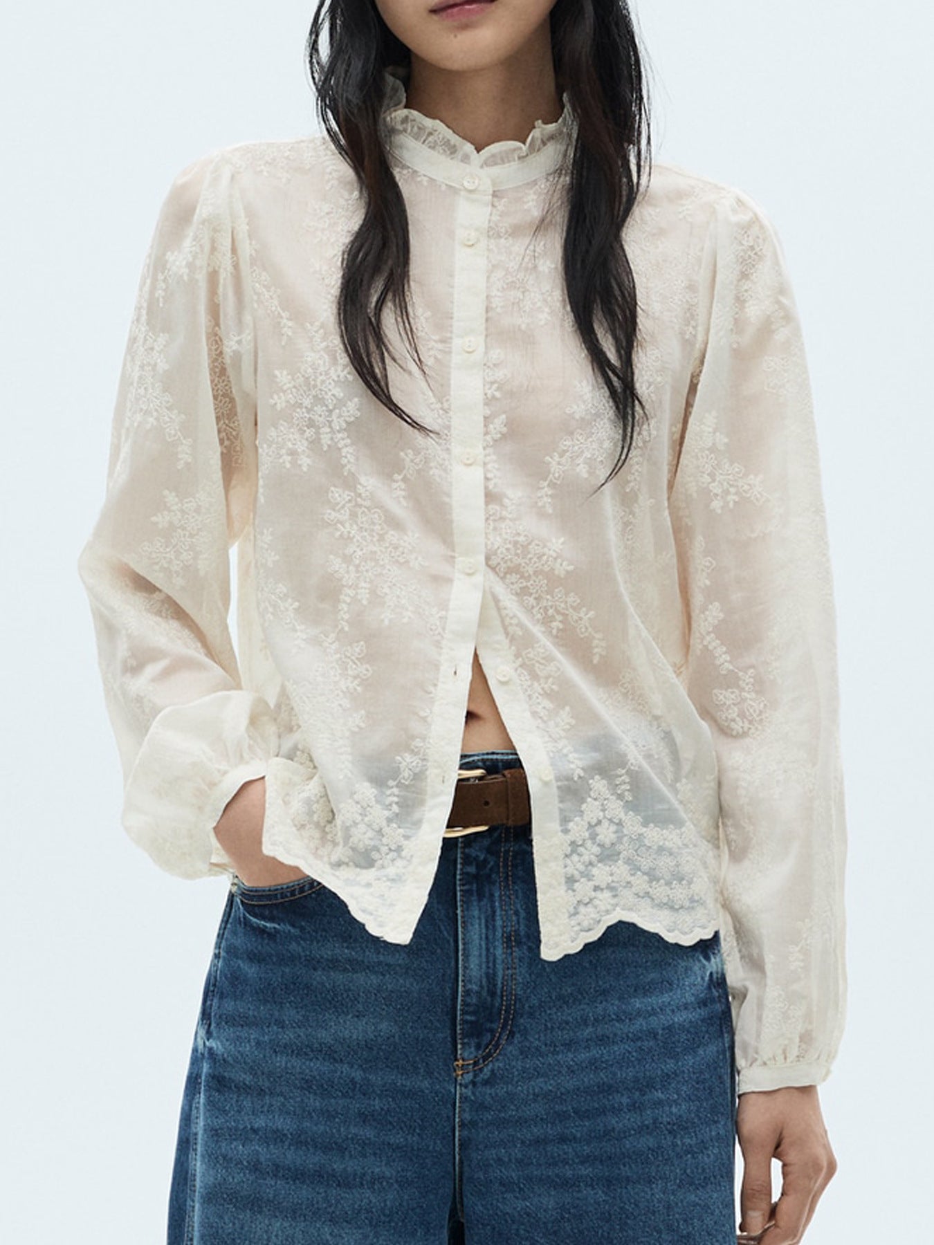 NEWYORKLISTED STYLE COLLECTION: Person wearing a sheer white lace blouse over a black top with blue jeans on a light gray background