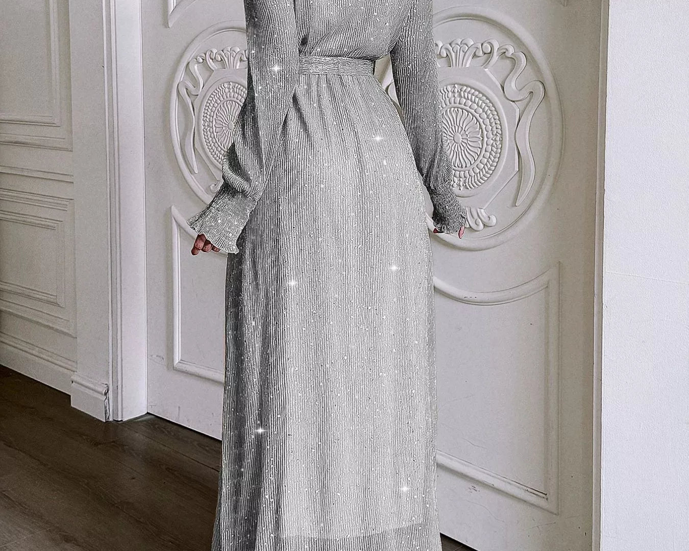 NEWYORKLISTED STYLE COLLECTION: Woman wearing a long, sparkly silver dress in a room with white paneled walls.