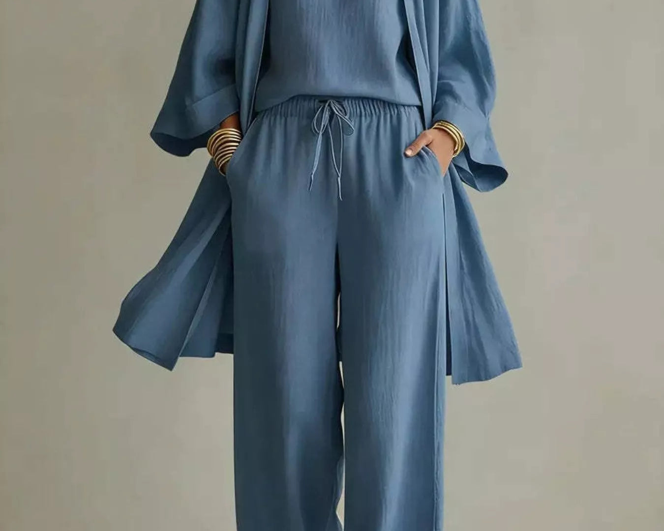 NEWYORKLISTED STYLE COLLECTION: A woman models a dusty blue linen-blend jumpsuit with a matching open-front cardigan. The jumpsuit features a V-neck, wide sleeves, a drawstring waist, and wide-leg pants.