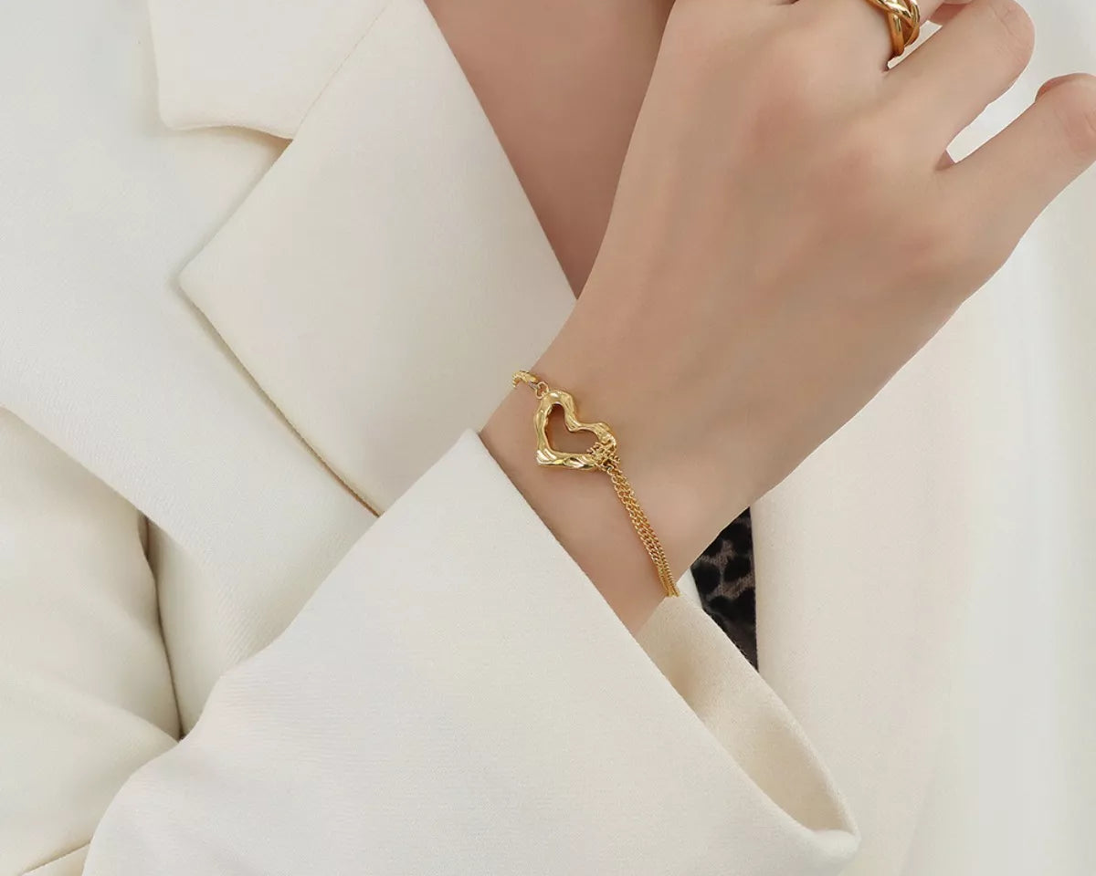 NYLD Glamour Collection by NEWYORKLISTED: Gold heart-shaped bracelet on a person wearing a white blazer.