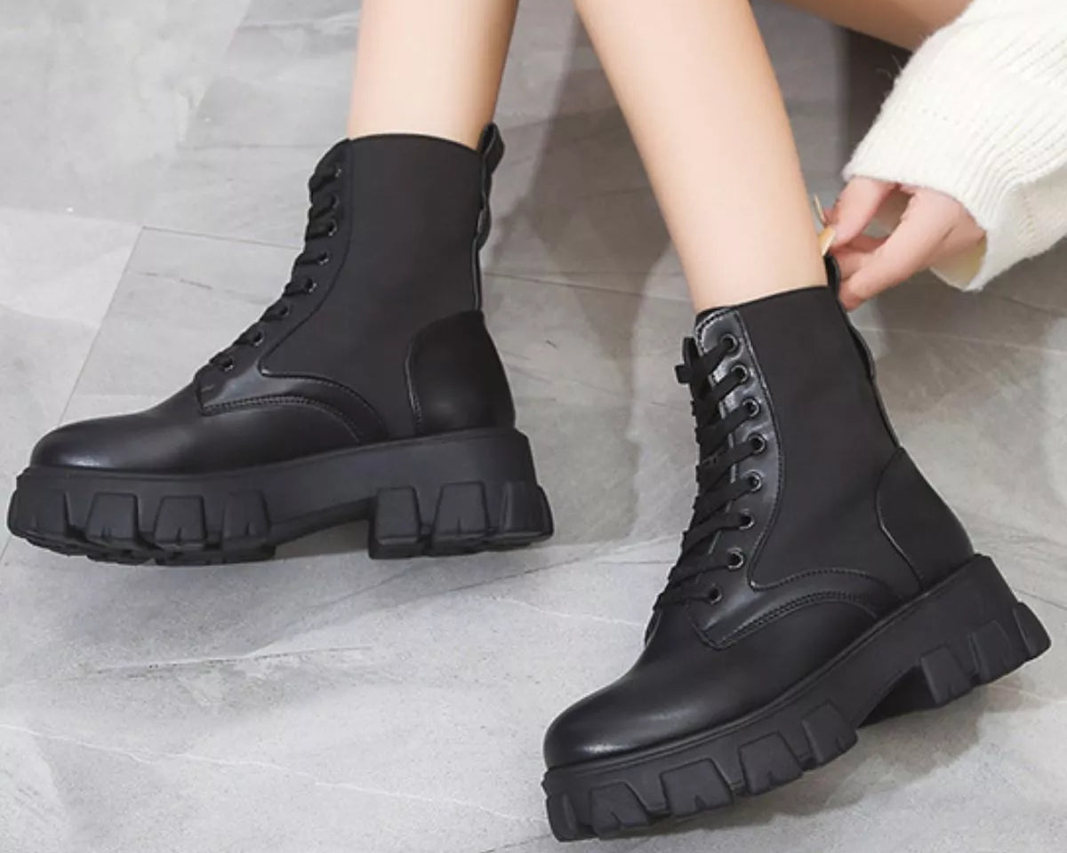NEWYORKLISTED SHOE COLLECTION: Black combat boots worn by a person on a gray floor