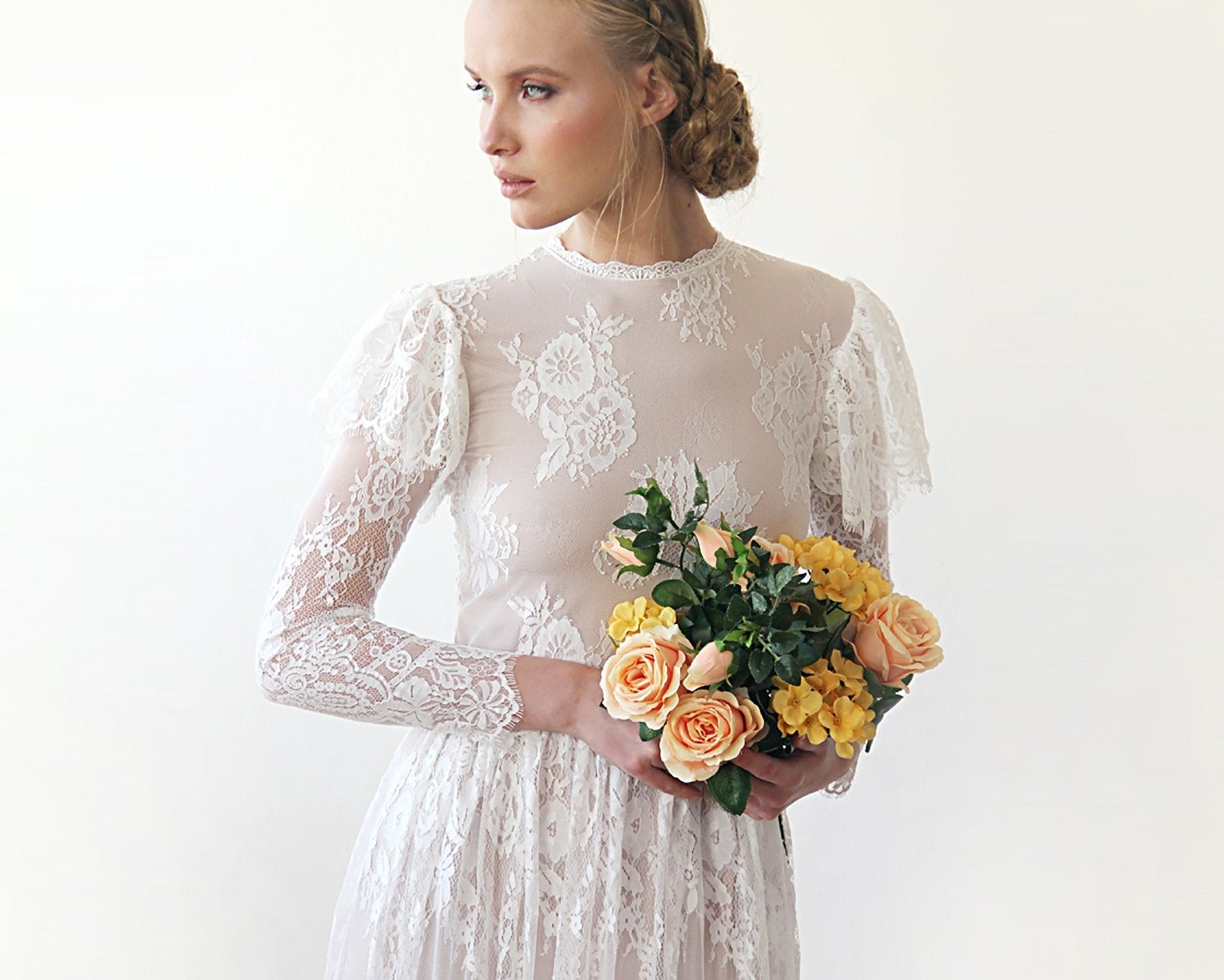 NEWYORKLISTED ELEGANT BRIDE COLLECTION: Woman in a white lace dress holding a bouquet of flowers against a plain background