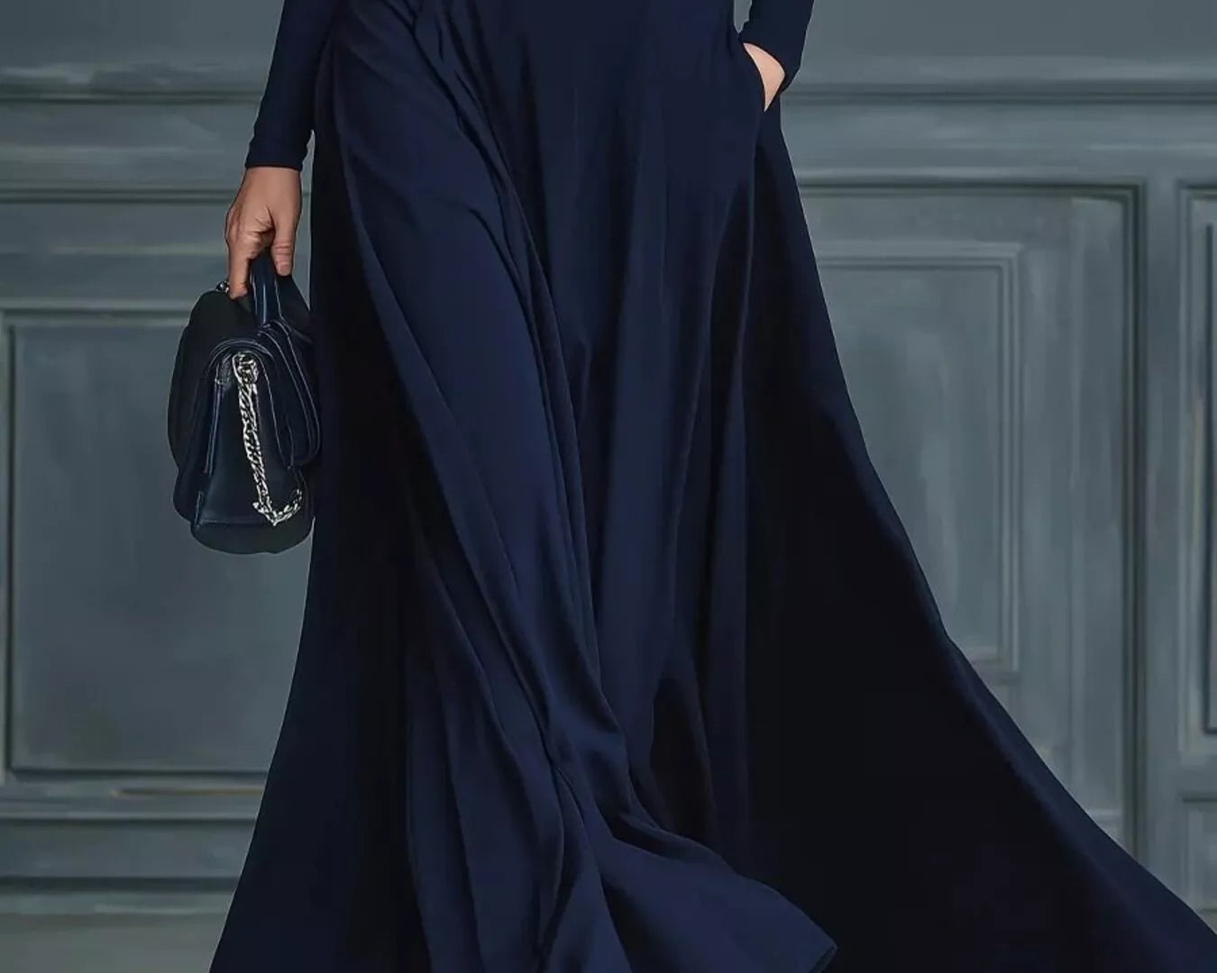 NEWYORKLISTED STYLE COLLECTION: Person wearing a long navy dress with a belt against a gray paneled wall.
