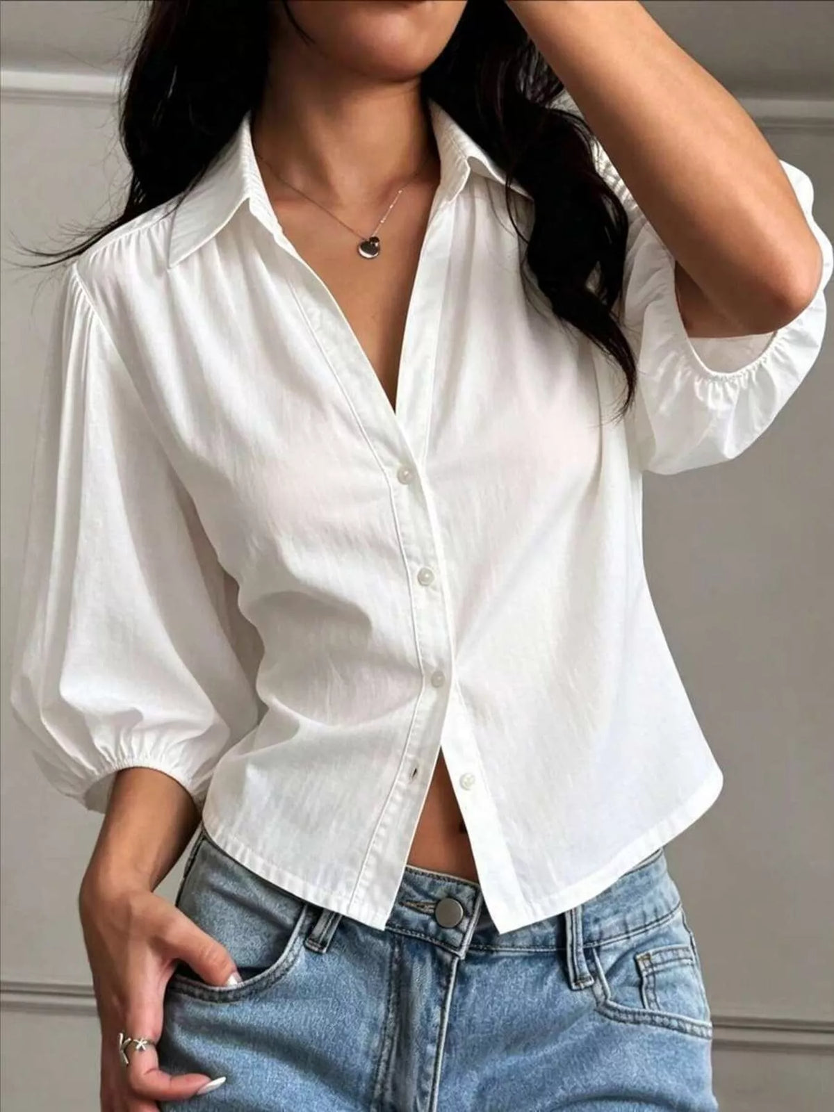 NEWYORKLISTED STYLE COLLECTION: A woman wearing a white short-sleeve button-up blouse with puff sleeves and light blue jeans, cropped from the mouth down to the hips.