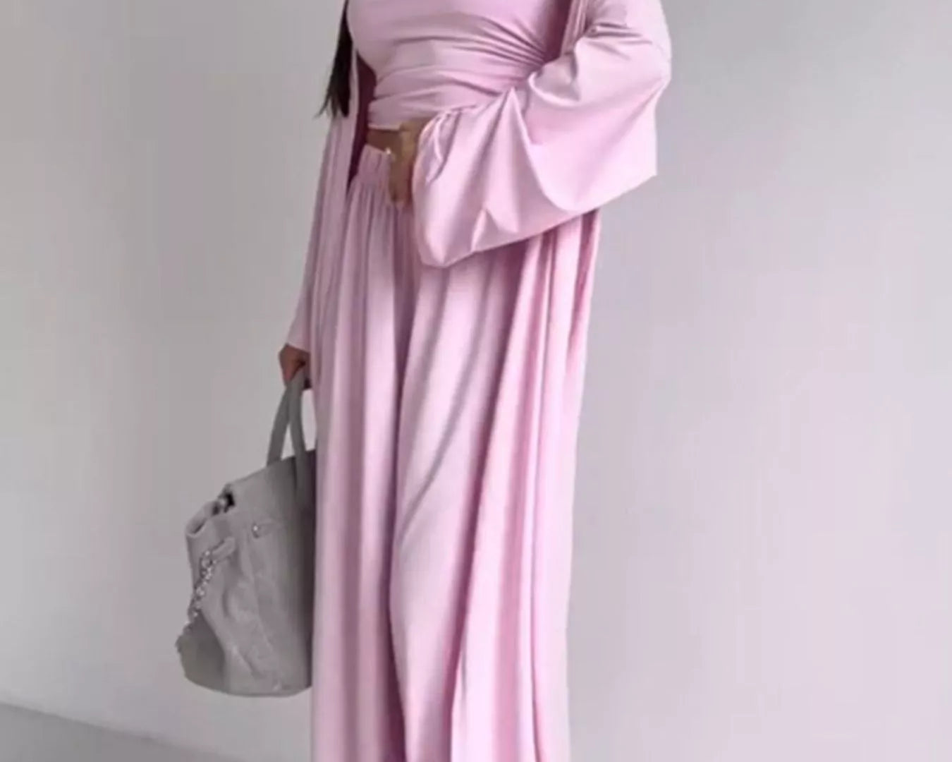 NEWYORKLISTED COMFORT COLLECTION: Woman wearing a pink off-shoulder dress holding a gray handbag against a white background