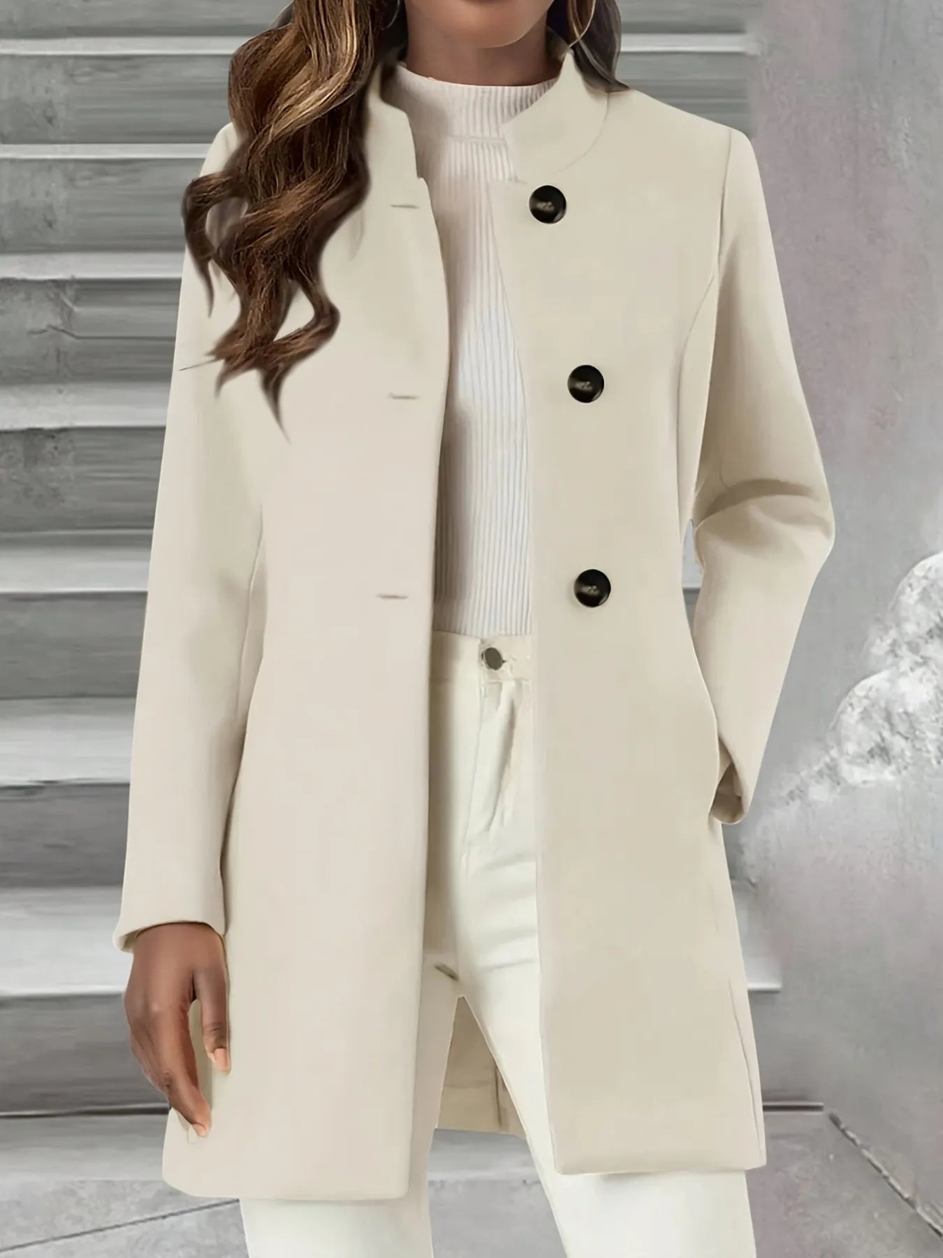 NEWYORKLISTED STYLE COLLECTION: Beige coat with black buttons worn by a person against a neutral background