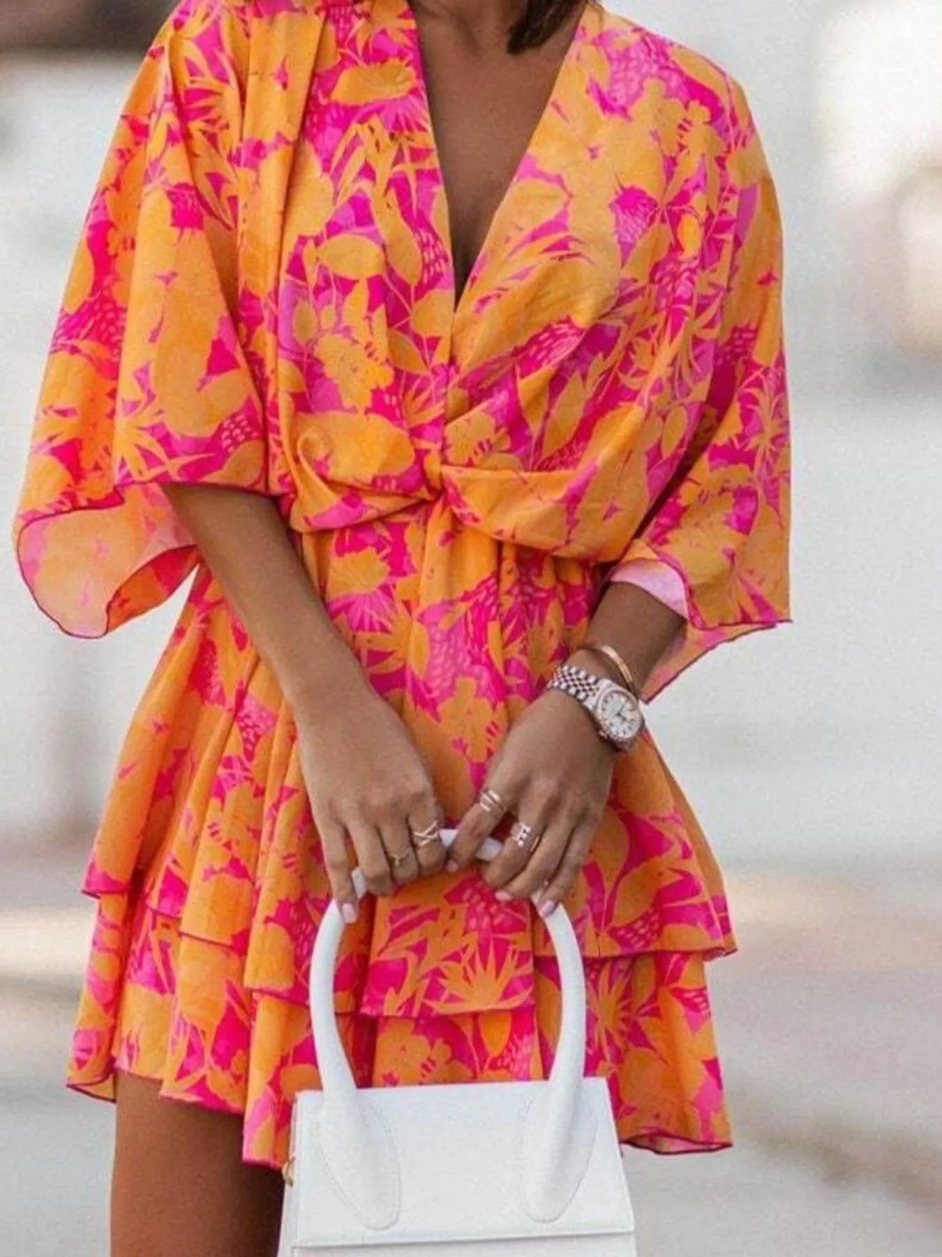 NEWYORKLISTED STYLE COLLECTION: Person wearing a bright orange and pink floral dress holding a white handbag.