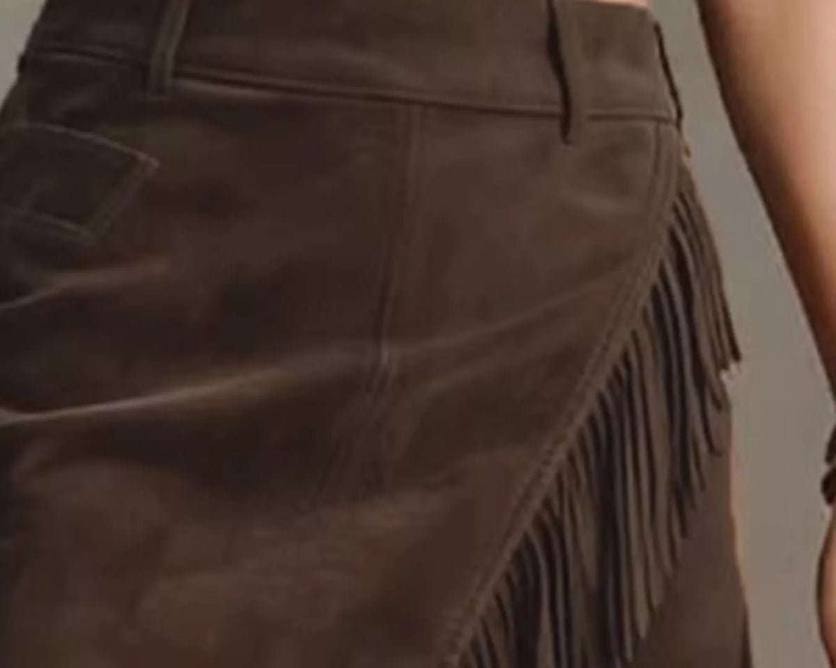 NEWYORKLISTED STYLE COLLECTION: A close-up of a dark brown suede skirt with diagonal fringe detailing, worn by a model in a cropped white top.