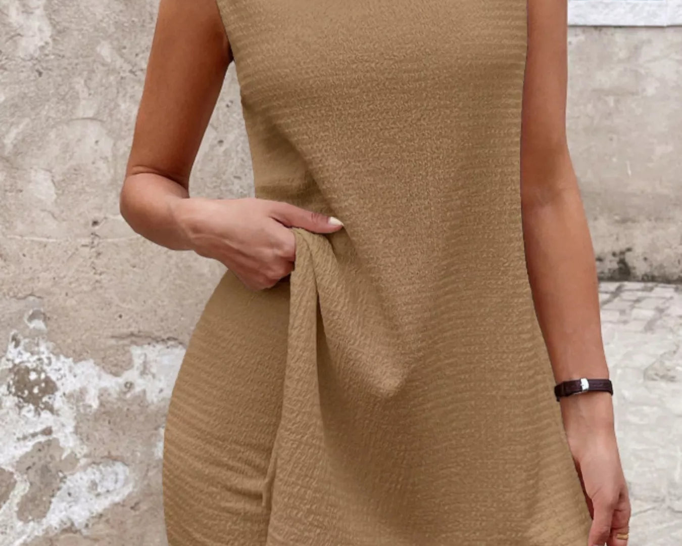 NEWYORKLISTED STYLE COLLECTION: Woman wearing a beige sleeveless top and shorts against a textured wall.