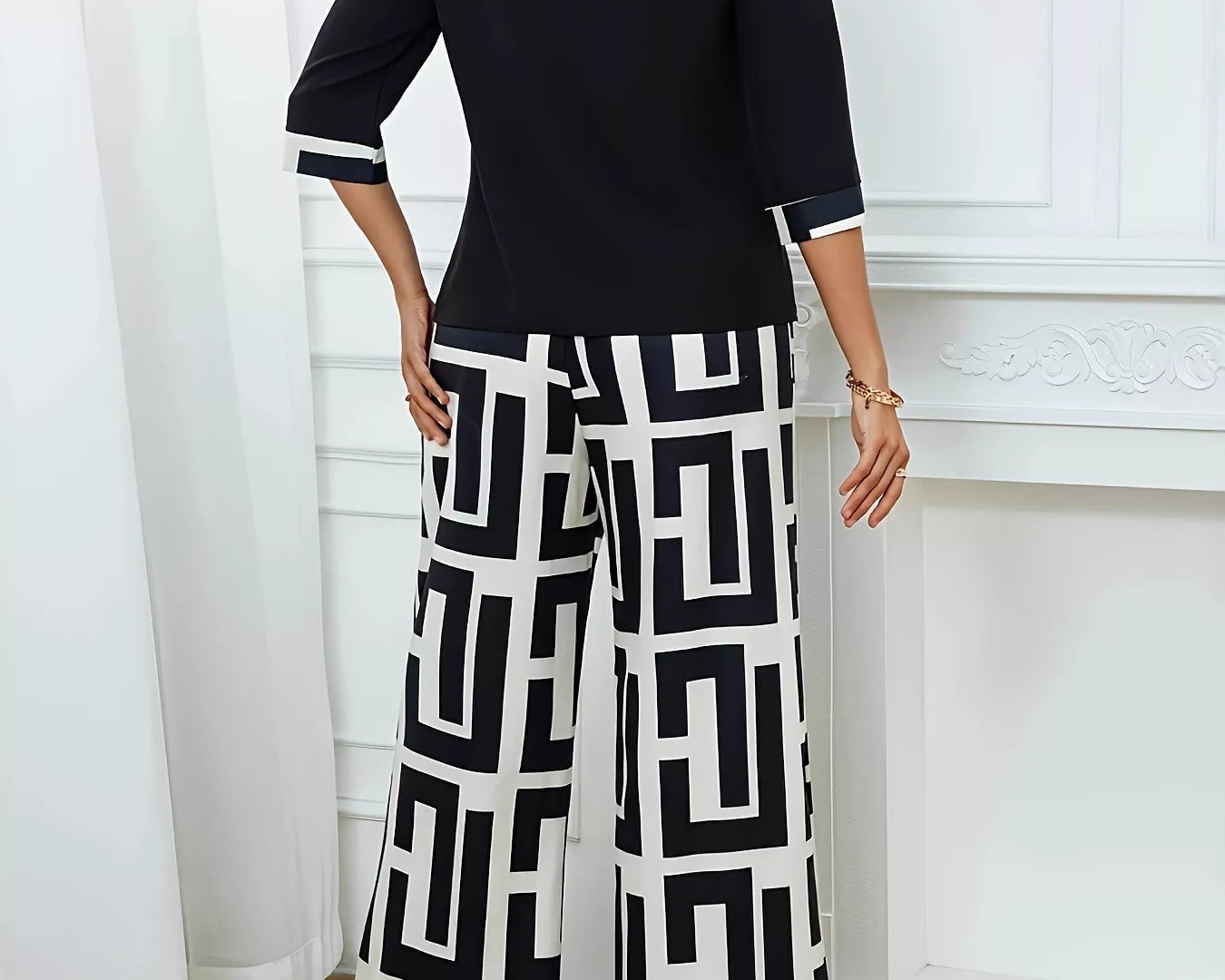 NEWYORKLISTED STYLE COLLECTION: Woman wearing a black top and geometric-patterned pants in a room with white curtains and a fireplace.
