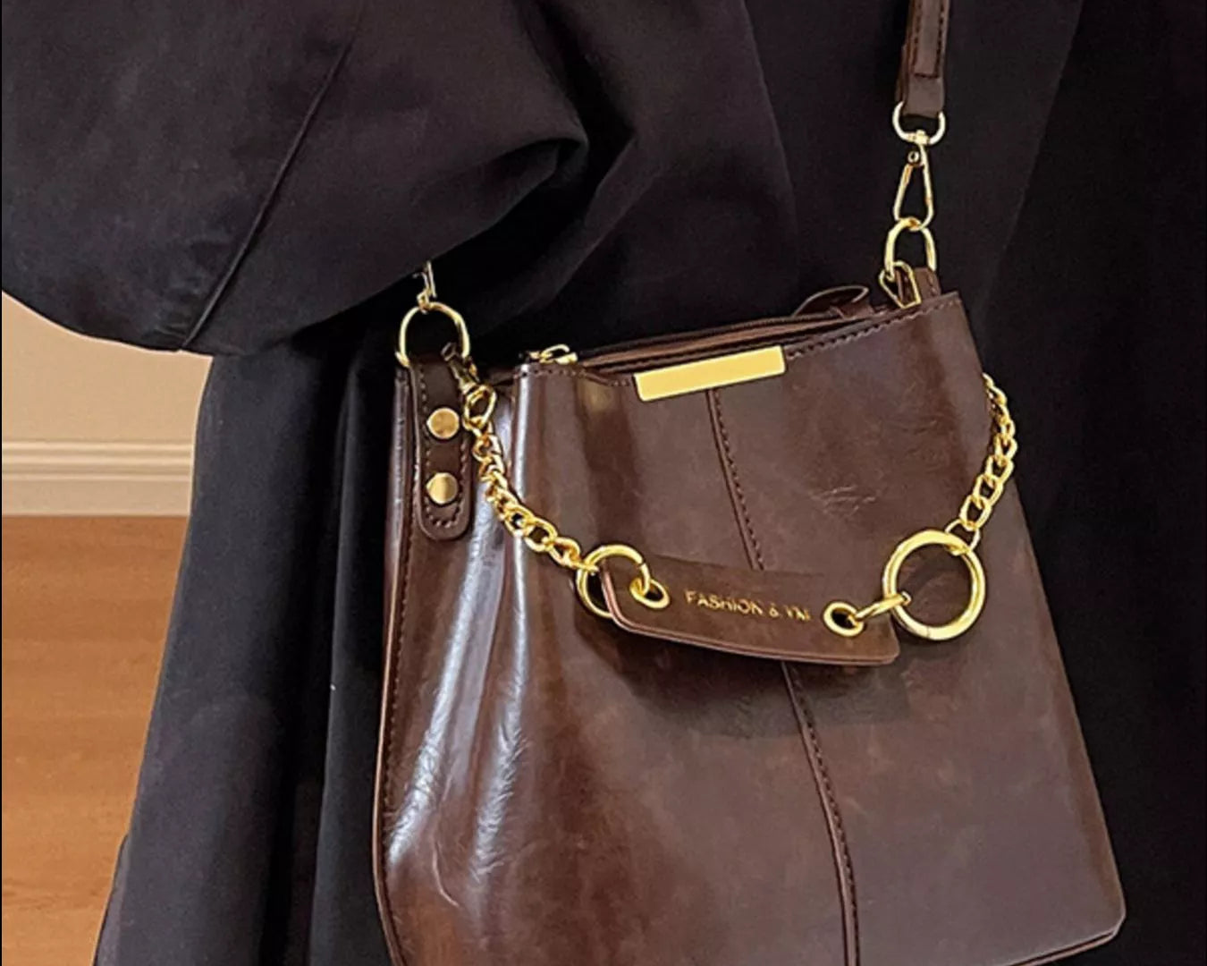 Brown leather handbag with gold chain strap held by a person wearing a dark coat. New York Listed Style Collection