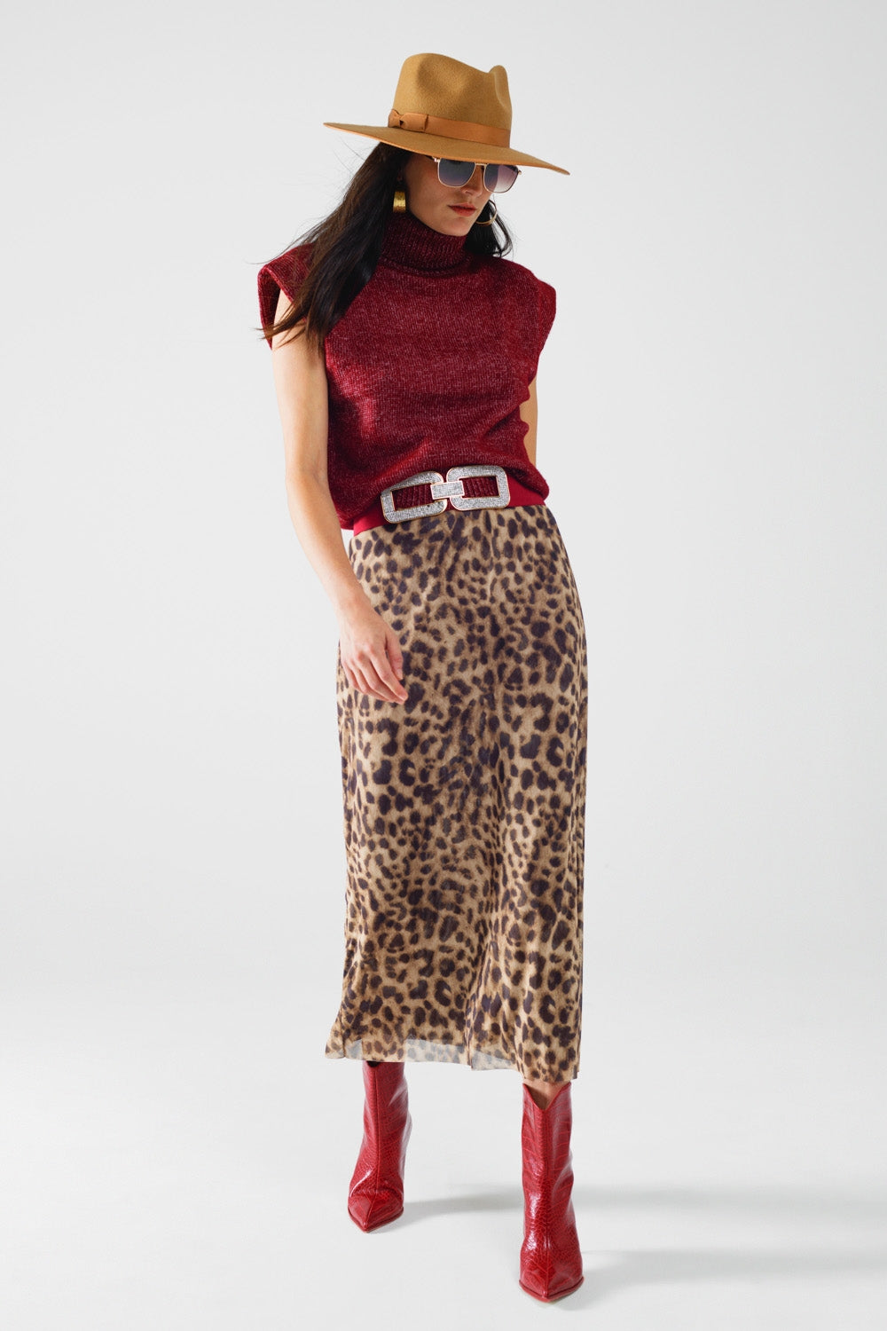 Woman wearing a red sleeveless top, leopard print skirt, red boots, and a brown hat on a white background