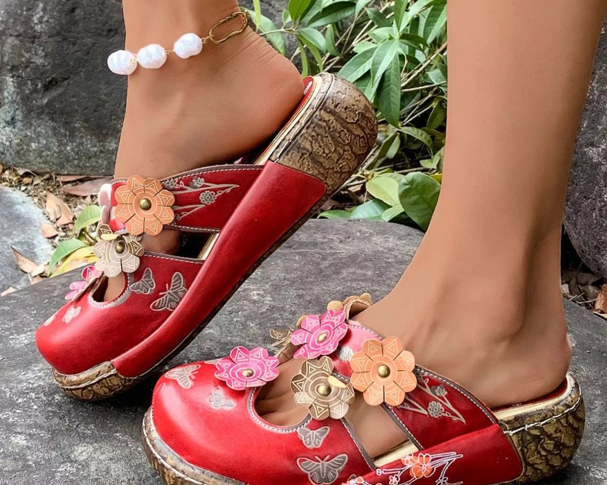 NEWYORKLISTED SHOE COLLECTION: Red floral embellished shoes worn on a stone surface with greenery in the background