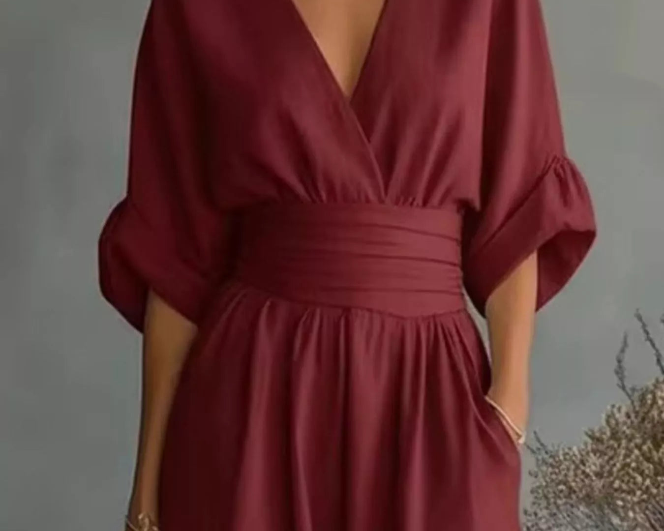 NEWYORKLISTED STYLE COLLECTION: A woman wearing a deep burgundy wrap-style dress with a V-neckline, gathered waist, and elbow-length puff sleeves, standing against a soft gray studio background.
