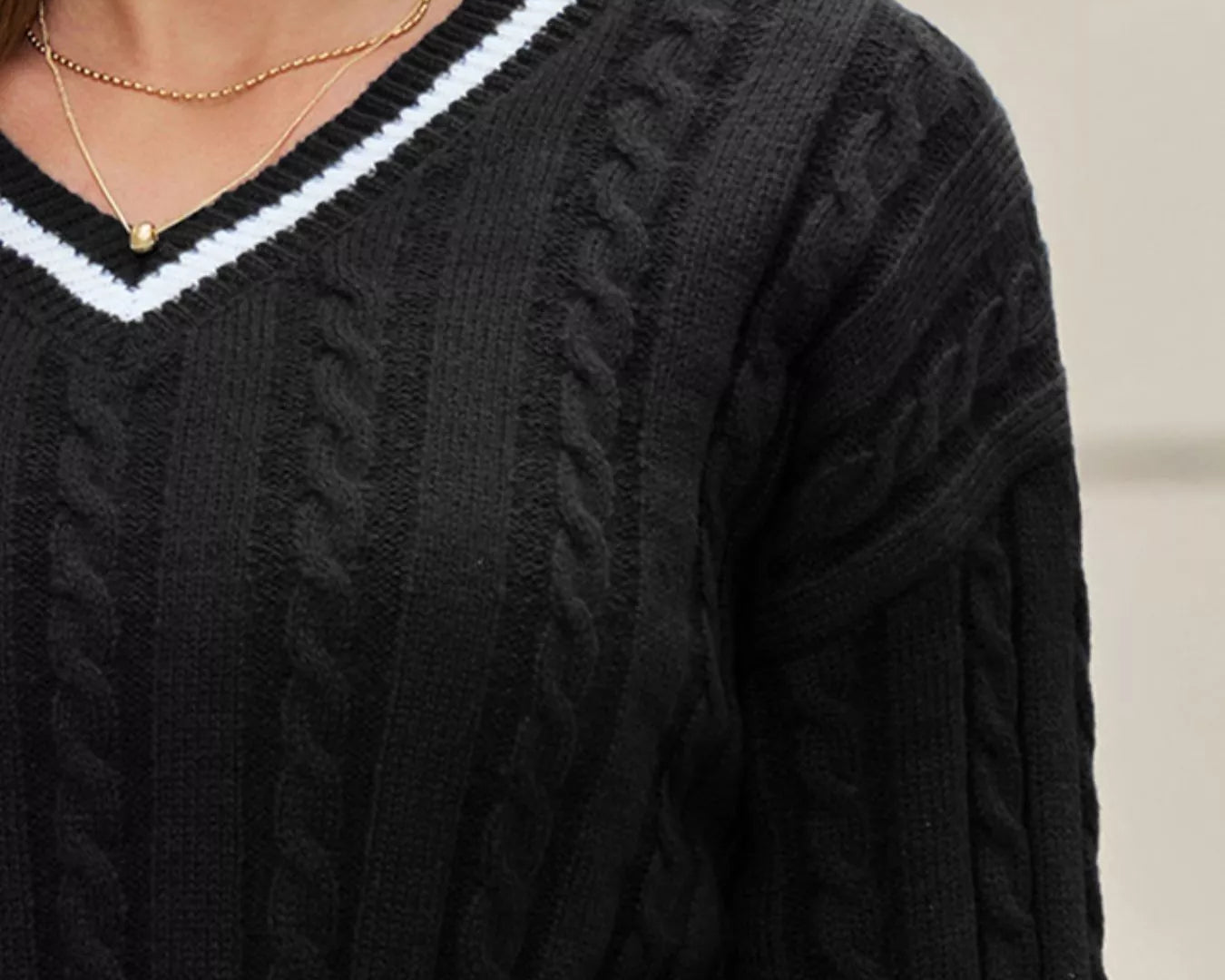 NEWYORKLSITED STYLE COLLECTION: Black cable knit sweater with white trim worn by a person.
