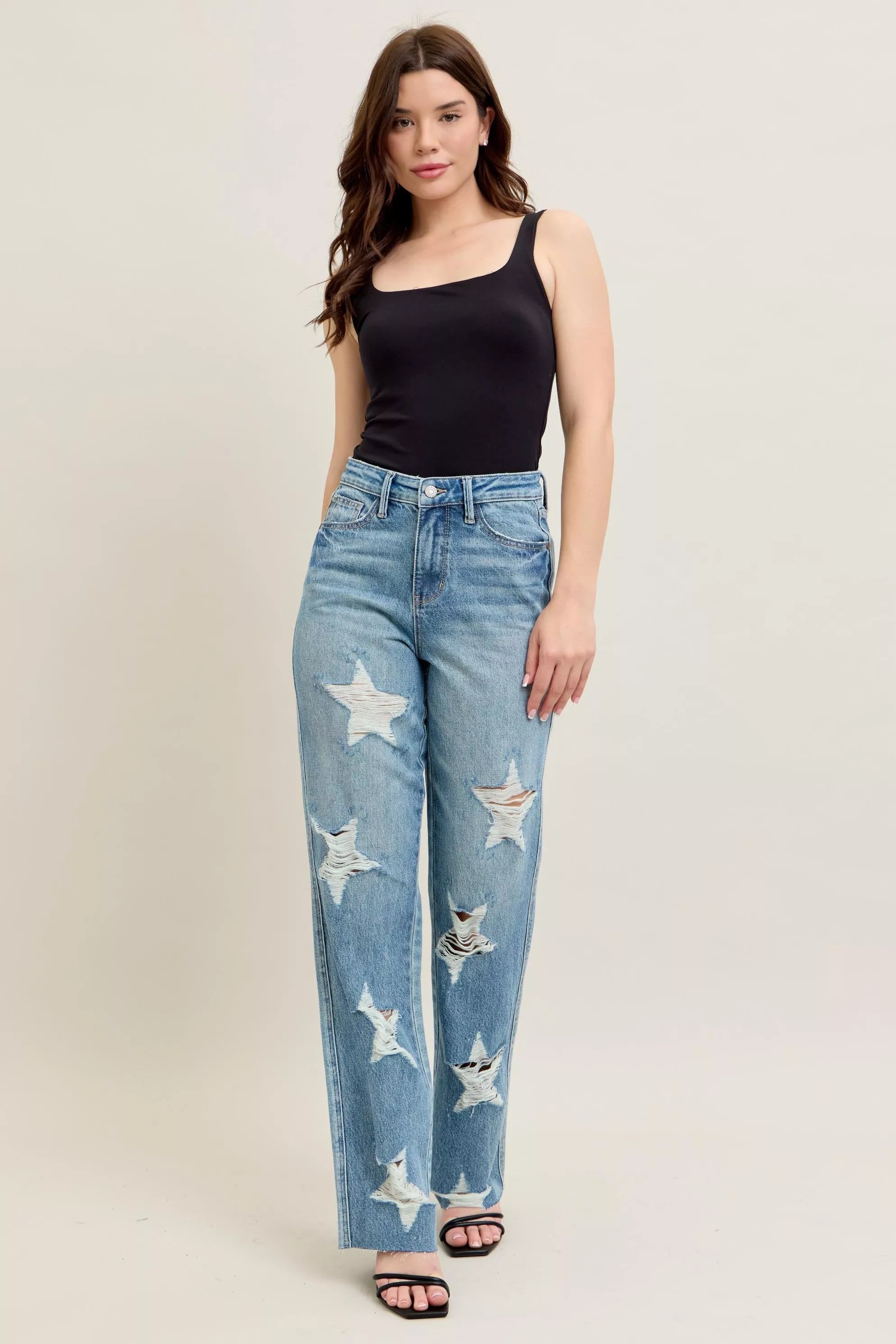 NEWYORKLISTED STYLE COLLECTION: Woman wearing blue jeans with star patterns and a black top on a beige background