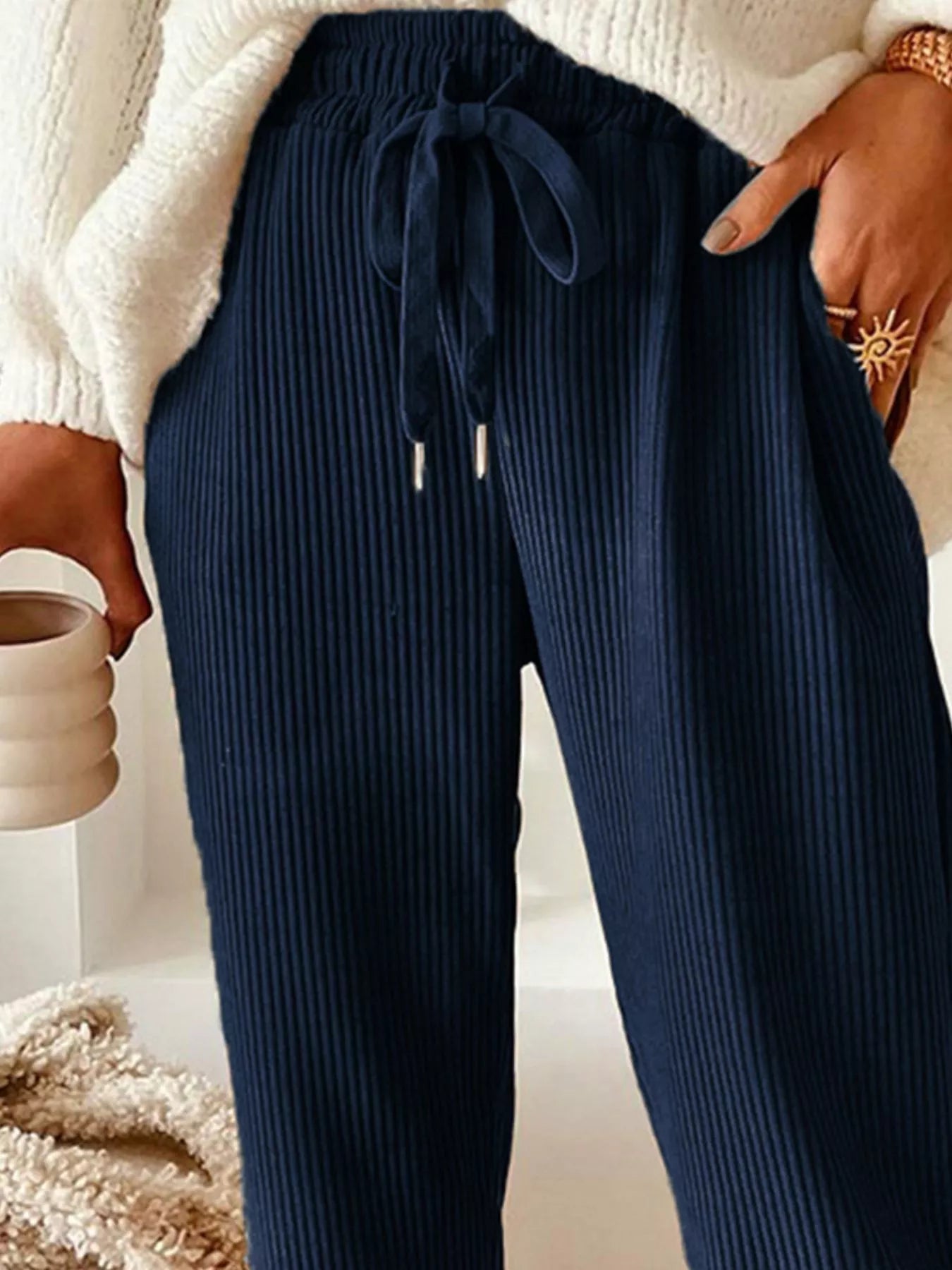 NEWYORKLISTED STYLE COLLECTION: Navy ribbed pants worn with a white sweater, held by a person.