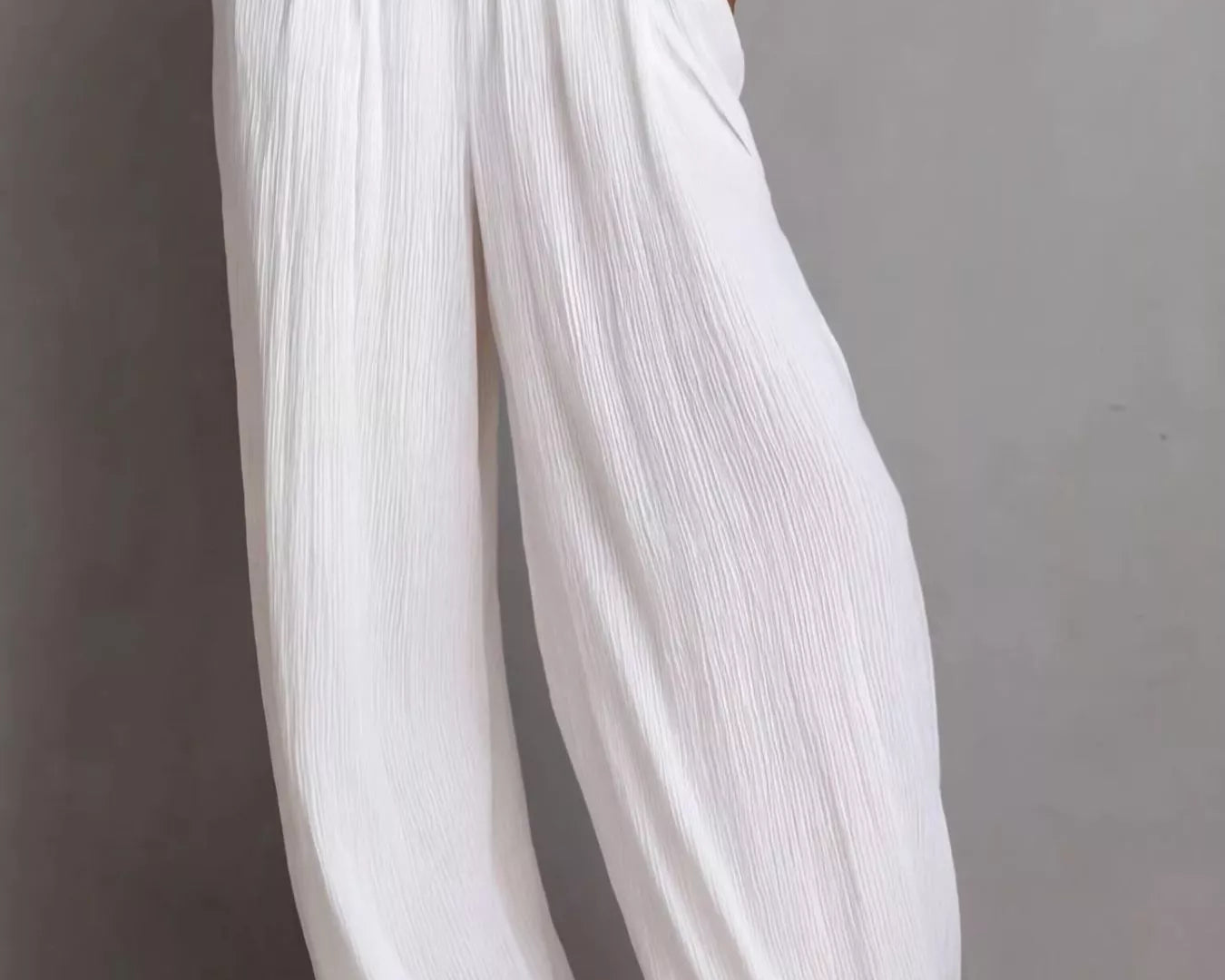 NEWYORKLISTED STYLE COLLECTION: White pleated pants worn by a person on a gray background