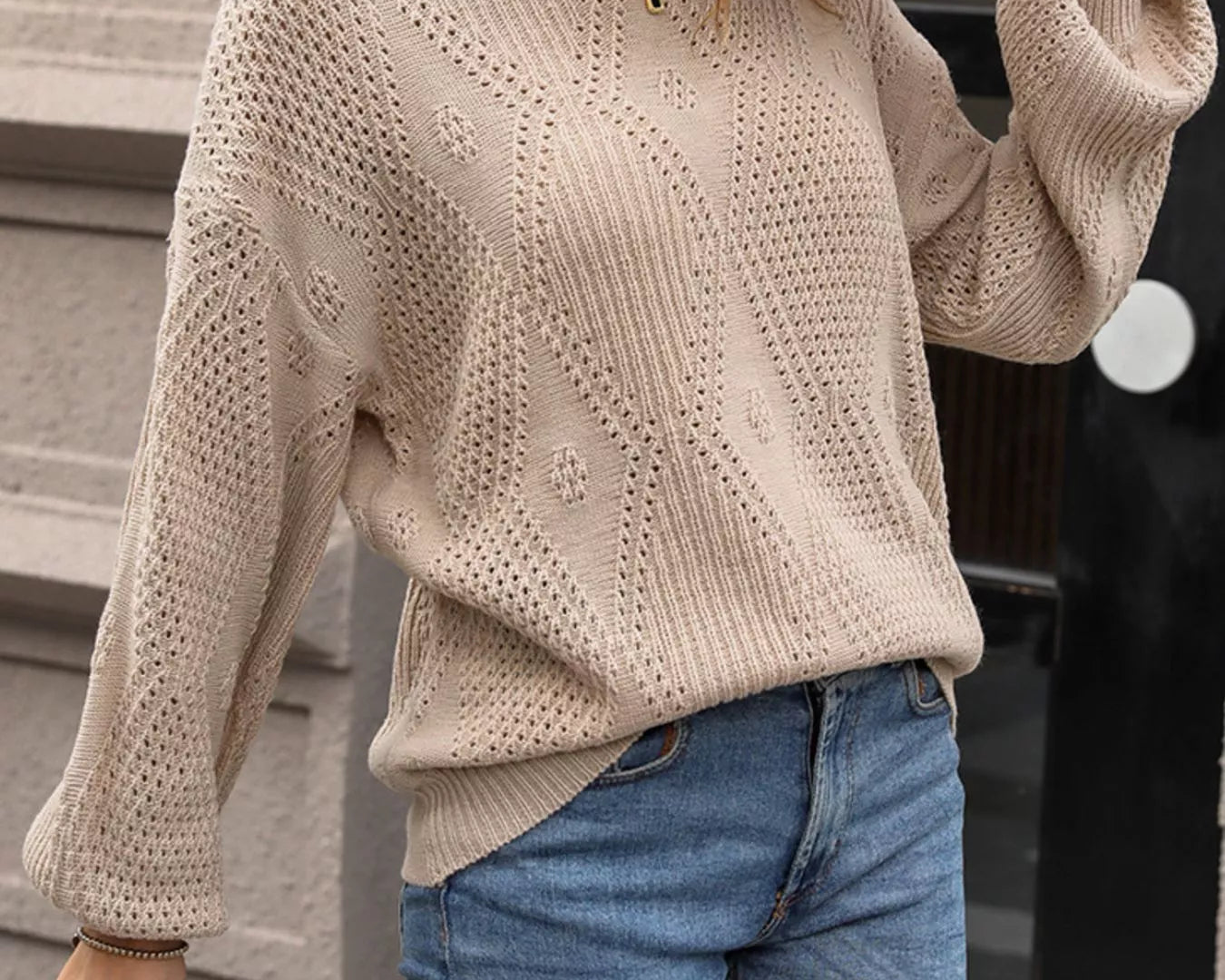 NEWYORKLISTED STYLE COLLECTION: Person wearing a beige knitted sweater and blue jeans, standing outdoors.