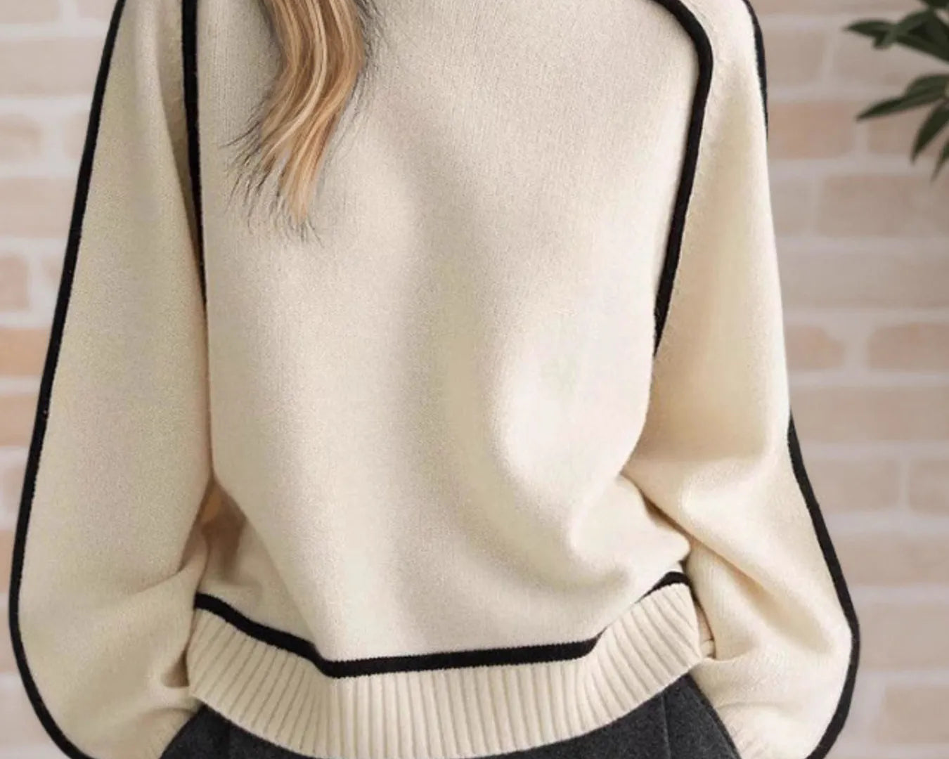NEWYORKLISTED STYLE COLLECTION: Person wearing a cream sweater with black trim against a brick wall.