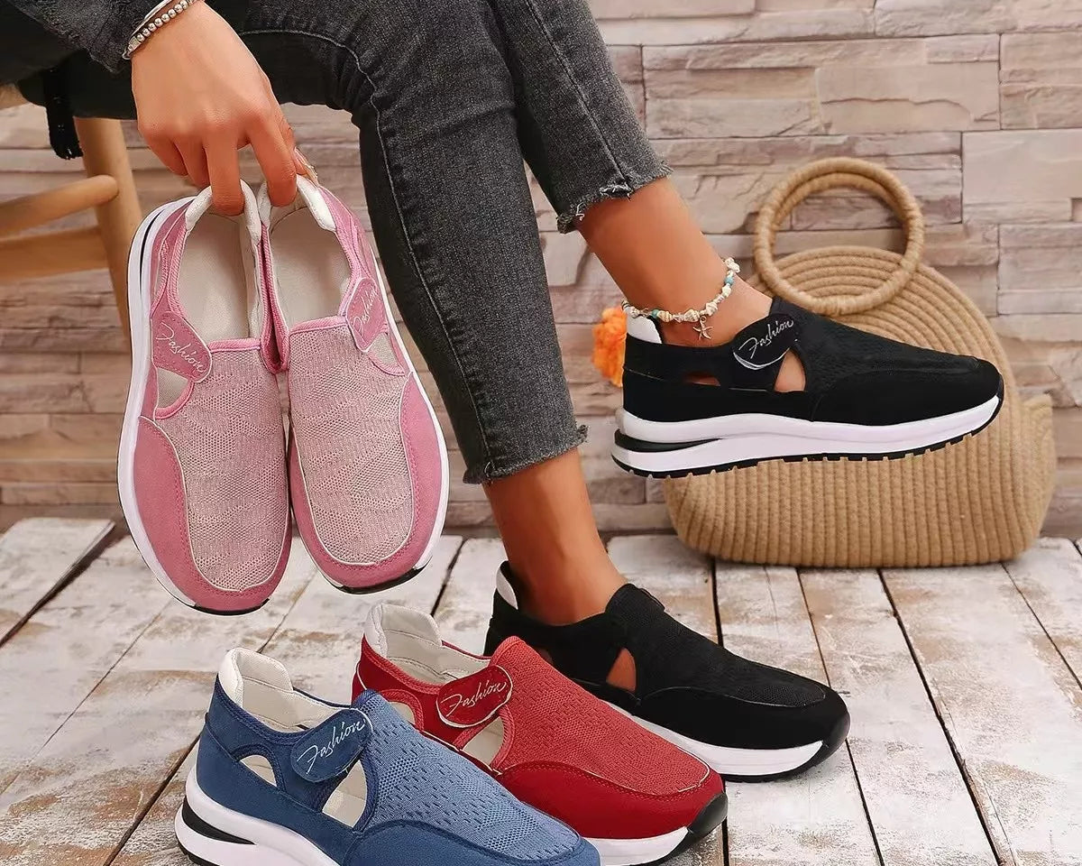 NEWYORKLISTED SHOE COLLECTION: Four women's slip-on platform sneakers in pink, blue, red, and black are displayed on a wooden floor, with a model holding the pink pair and wearing the black pair. A woven straw bag and a faux-stone wall backdrop complete the scene.