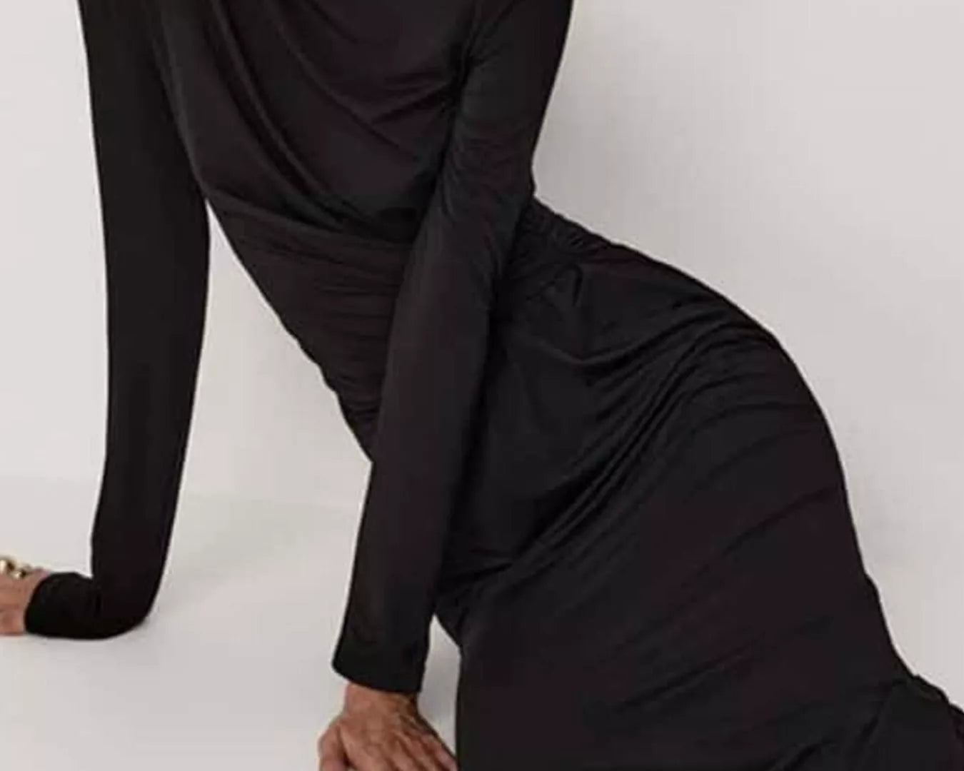 NEWYORKLISTED STYLE COLLECTION: Model is wearing a black long-sleeve dress sitting on a white floor.