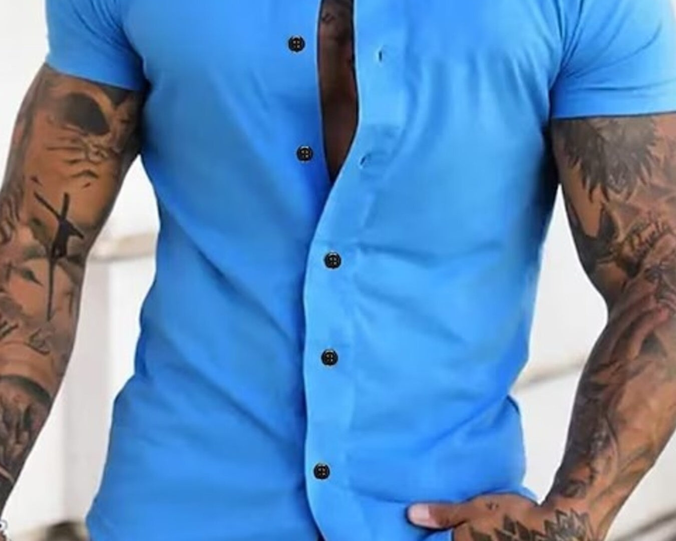 NEWYORKLISTED ATLAS MEN's COLLECTION: Man wearing a blue short-sleeve button-up shirt with tattoos on arms.