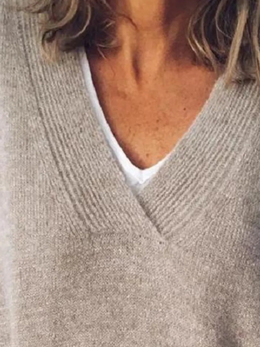 NEWYORKLISTED STYLE COLLECTION: Close-up of a person wearing a beige sweater over a white shirt.