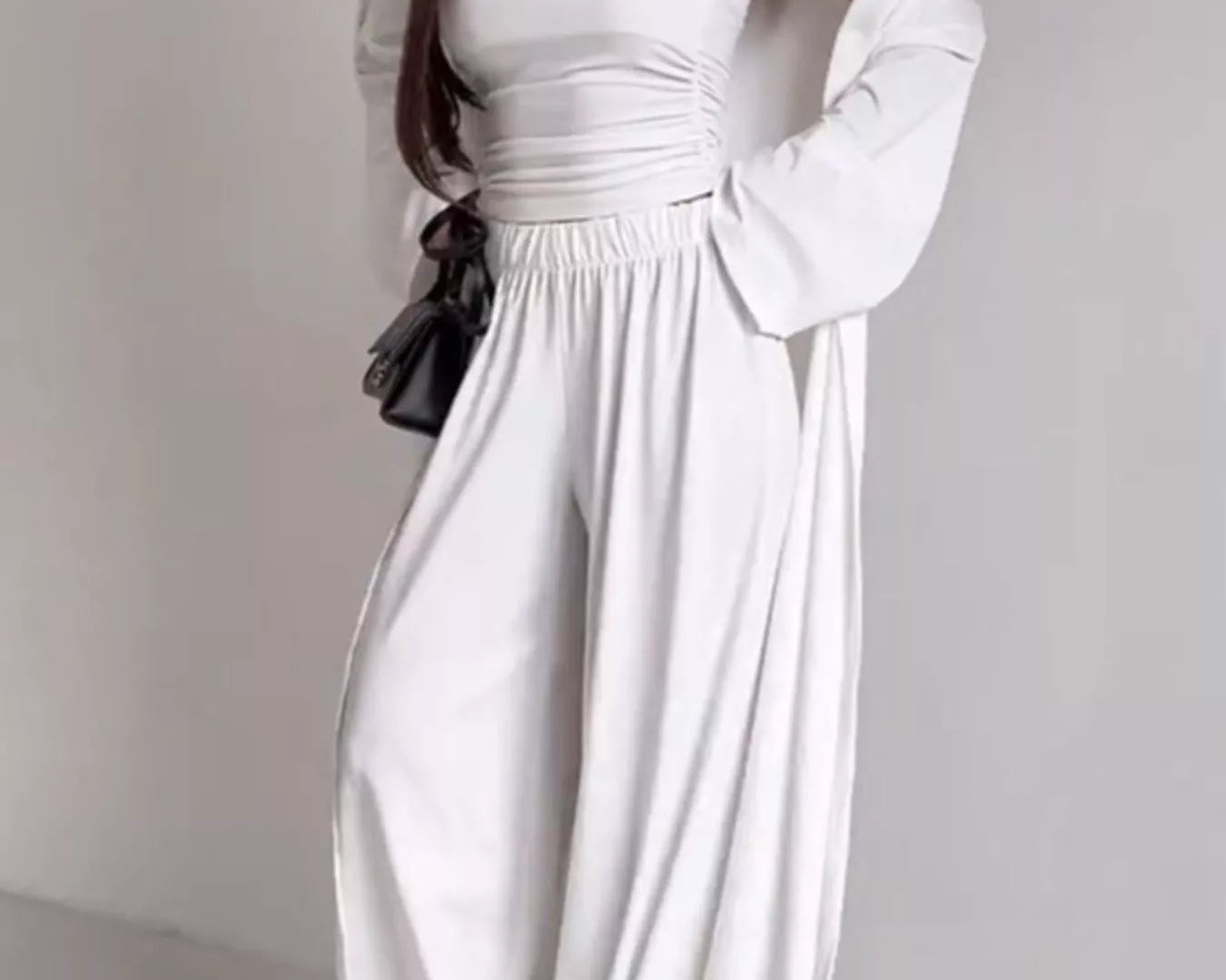 NEWYORKLISTED COMFORT COLLECTION: Woman wearing a white off-shoulder dress with long sleeves on a plain background