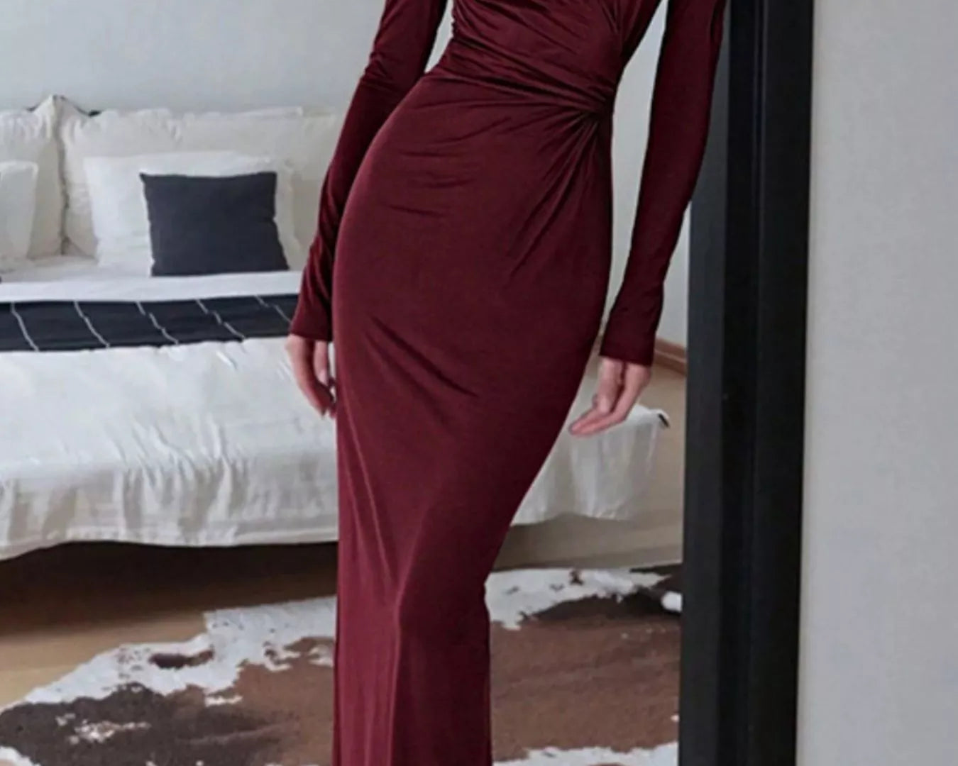 NEWYORKLISTED STYLE COLLECTION: Person wearing a burgundy dress standing in a room with a bed and cowhide rug.