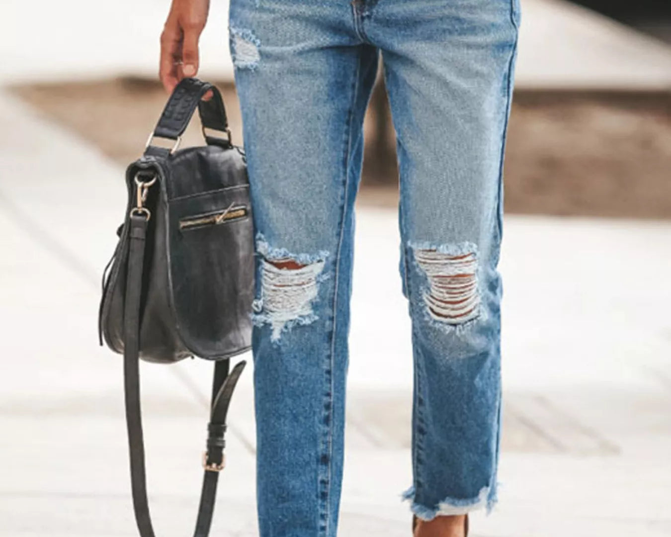 NEWYORKLISTED STYLE COLLECTION: Person wearing distressed blue jeans with a black handbag on a blurred background