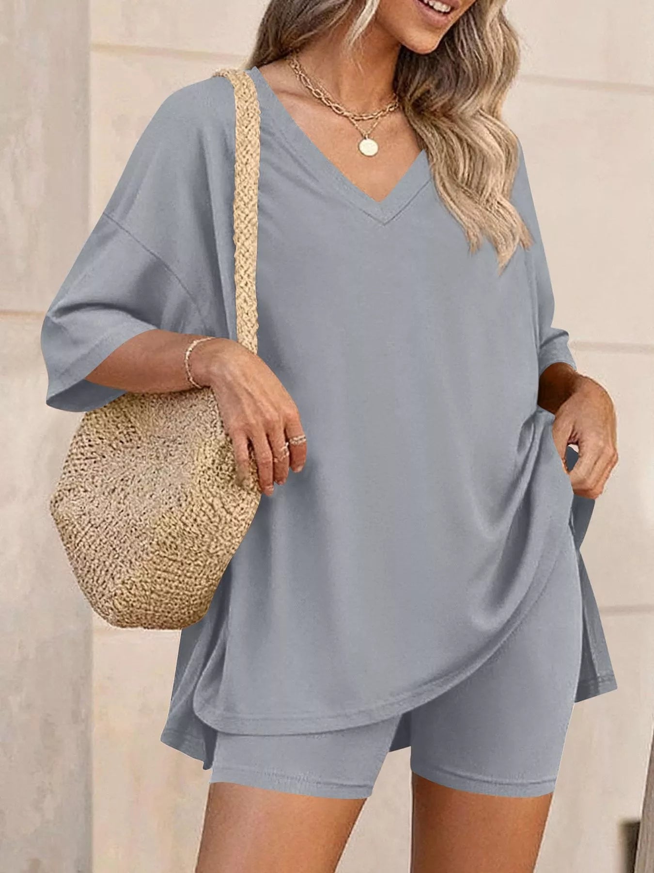 NEWYORKLISTED COMFORT COLLECTION: Woman wearing a gray outfit with a straw bag against a neutral background