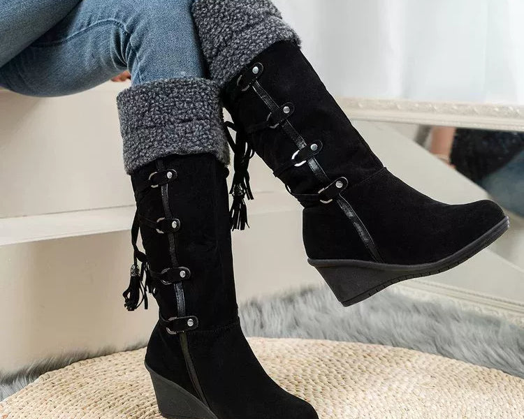 NEWYORKLISTED SHOE COLLECTION: Black wedge boots with lace-up design worn by a person sitting on a white surface.