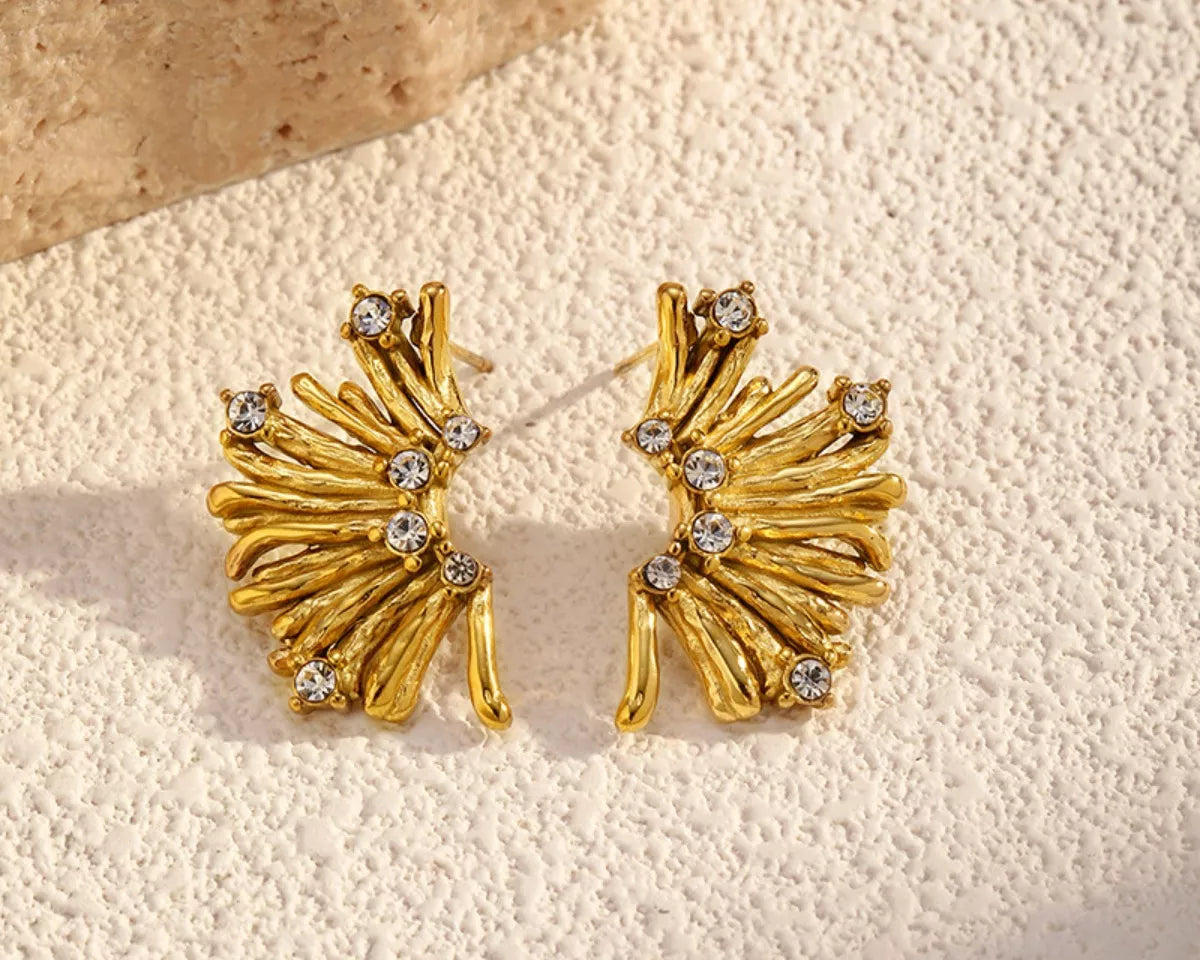 NYLD Glamour Collection by NEWYORKLISTED: Gold earrings with gemstones on a textured beige surface