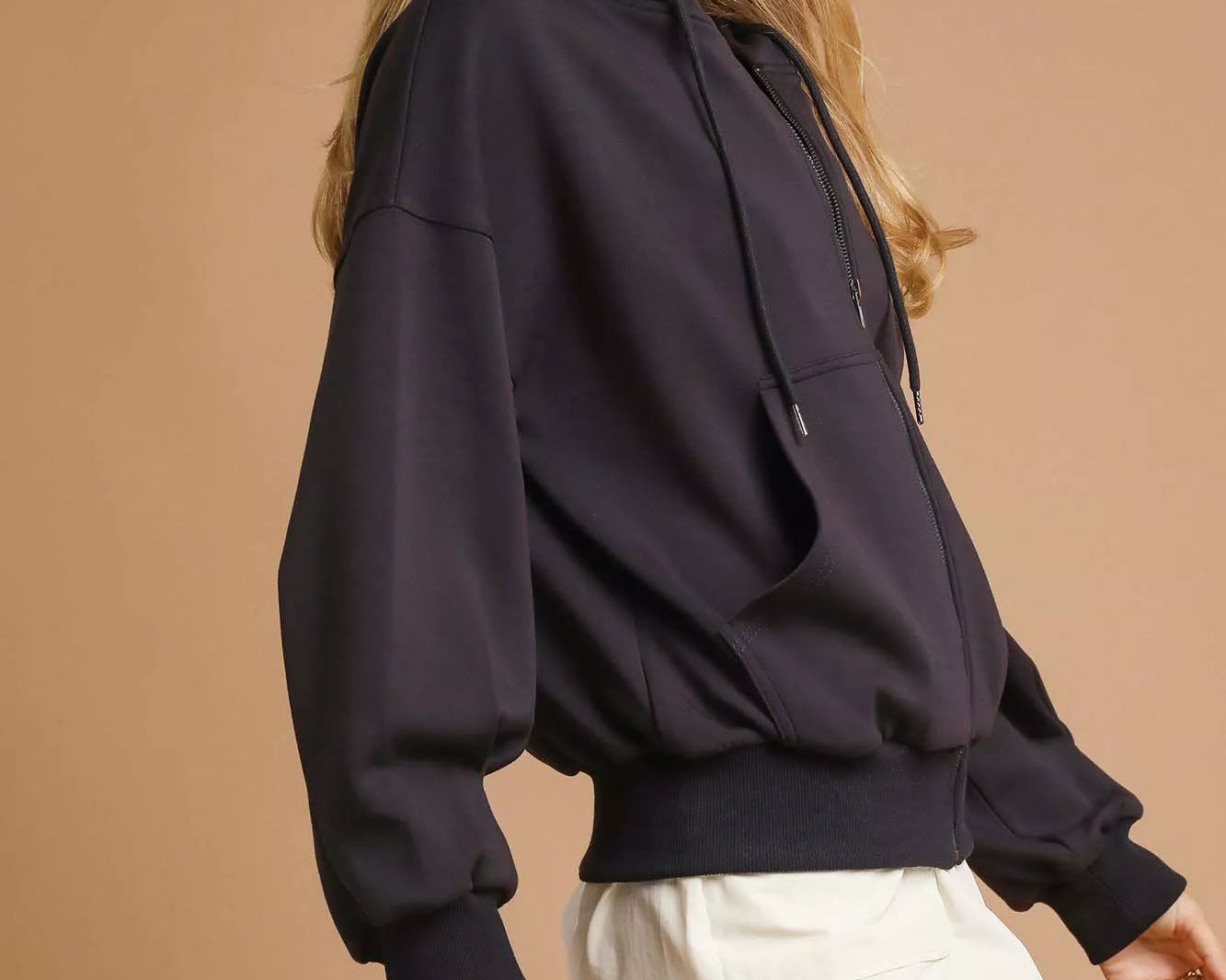 NEWYORKLISTED STYLE COLLECTION: Woman wearing a black hoodie and white shorts against a beige background