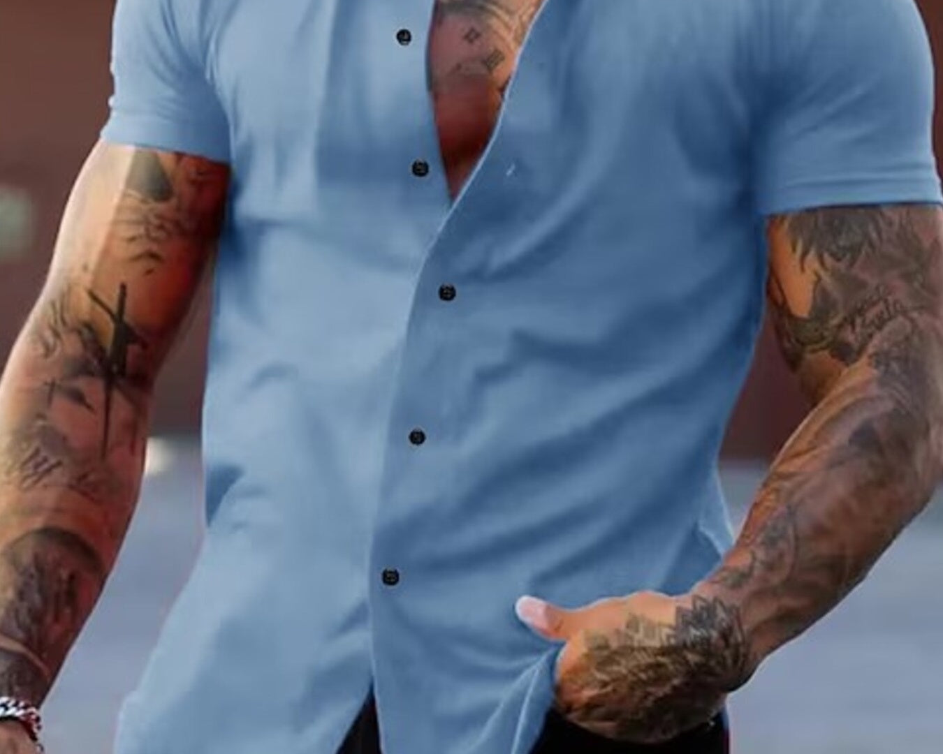 NEWYORKLISTED ATLAS MEN's COLLECTION: Man wearing a light blue button-up shirt with tattoos on arms, standing against a blurred background.