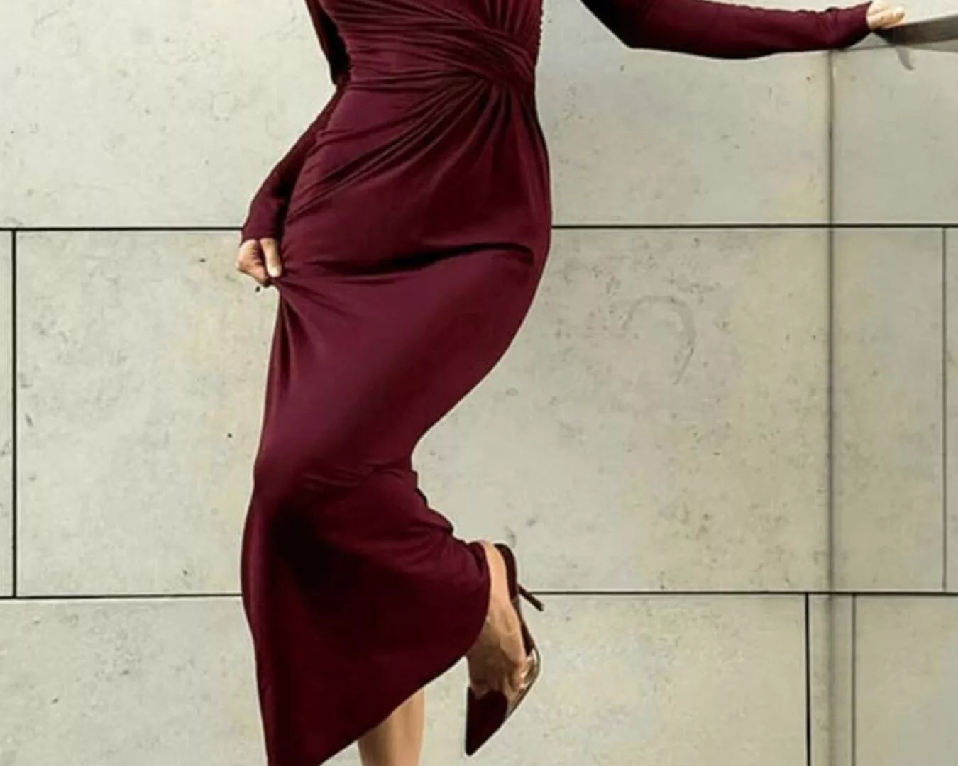 NEWYORKLISTED STYLE COLLECTION: Woman wearing a burgundy dress against a light-colored wall.