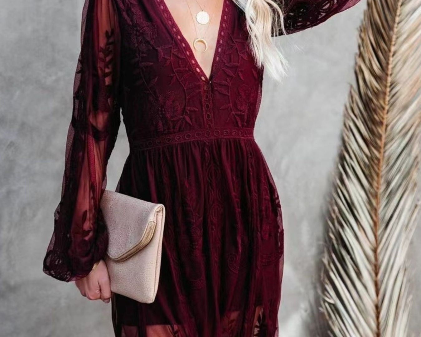 NEWYORKLISTED STYLE COLLECTION: Woman wearing a burgundy lace dress with long sleeves, holding a beige clutch against a neutral background.